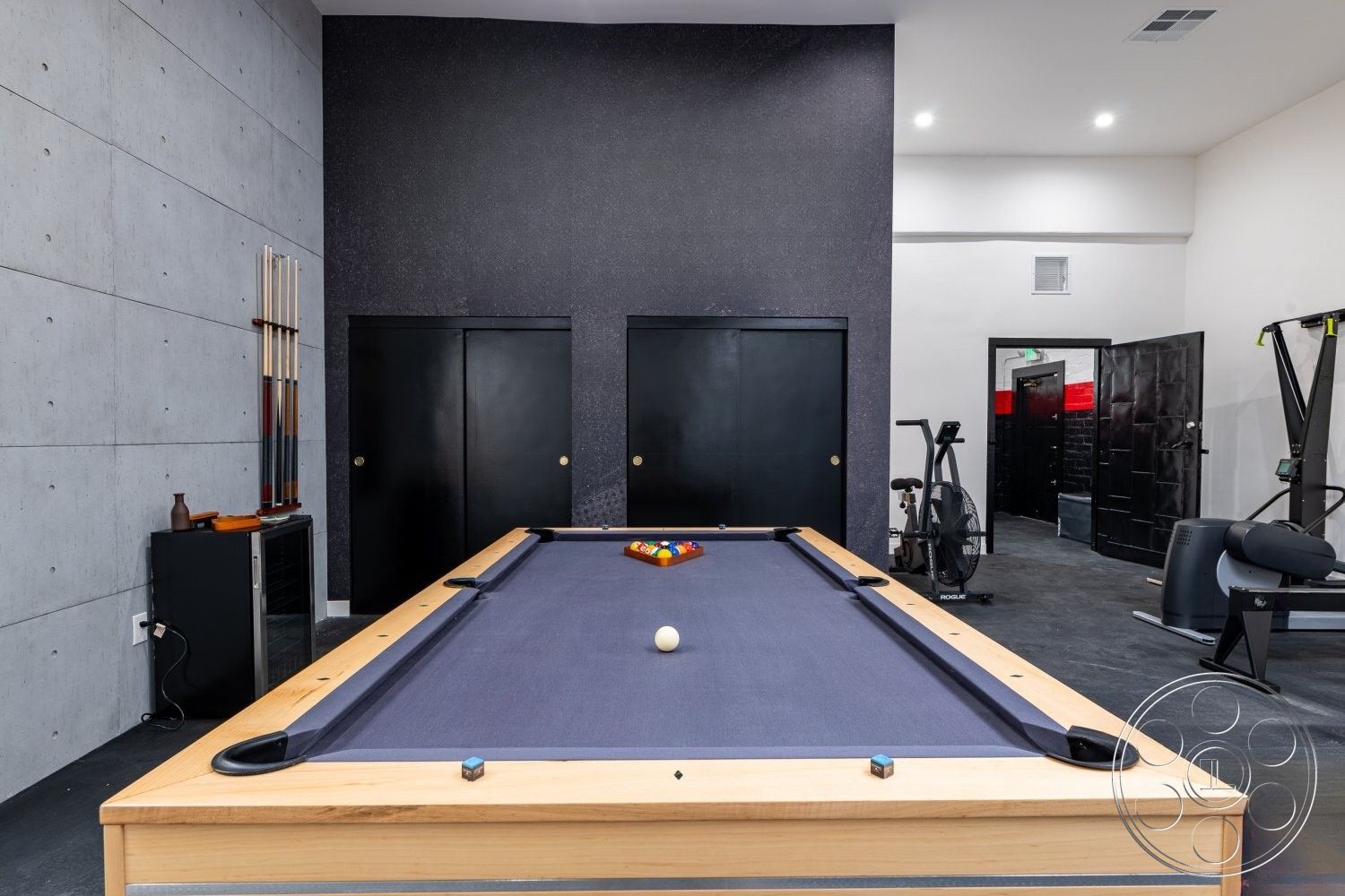 Office 125 - concrete walls interior, textured black accent wall interior, hardwood pool table construction, black wooden doors interior, dark concrete flooring interior, glass cabinet for billiard accessories, fitness area with exercise equipment interior, recessed ceiling lighting interior, powder-coated steel cabinets interior, modern minimalist design interior, game room layout interior, open-concept space interior