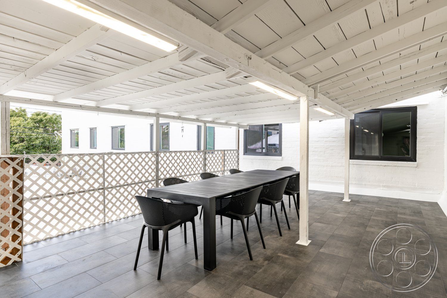 Office 125 - neutral color palette, modern design elements, urban setting, floor-to-ceiling windows, contemporary architecture, gray tile flooring, indoor-outdoor living, wood beam ceiling, open-air dining area, sunlit outdoor space, exterior deck space, black metal dining table, black plastic outdoor chairs, white painted wood railings, lattice wood privacy screen