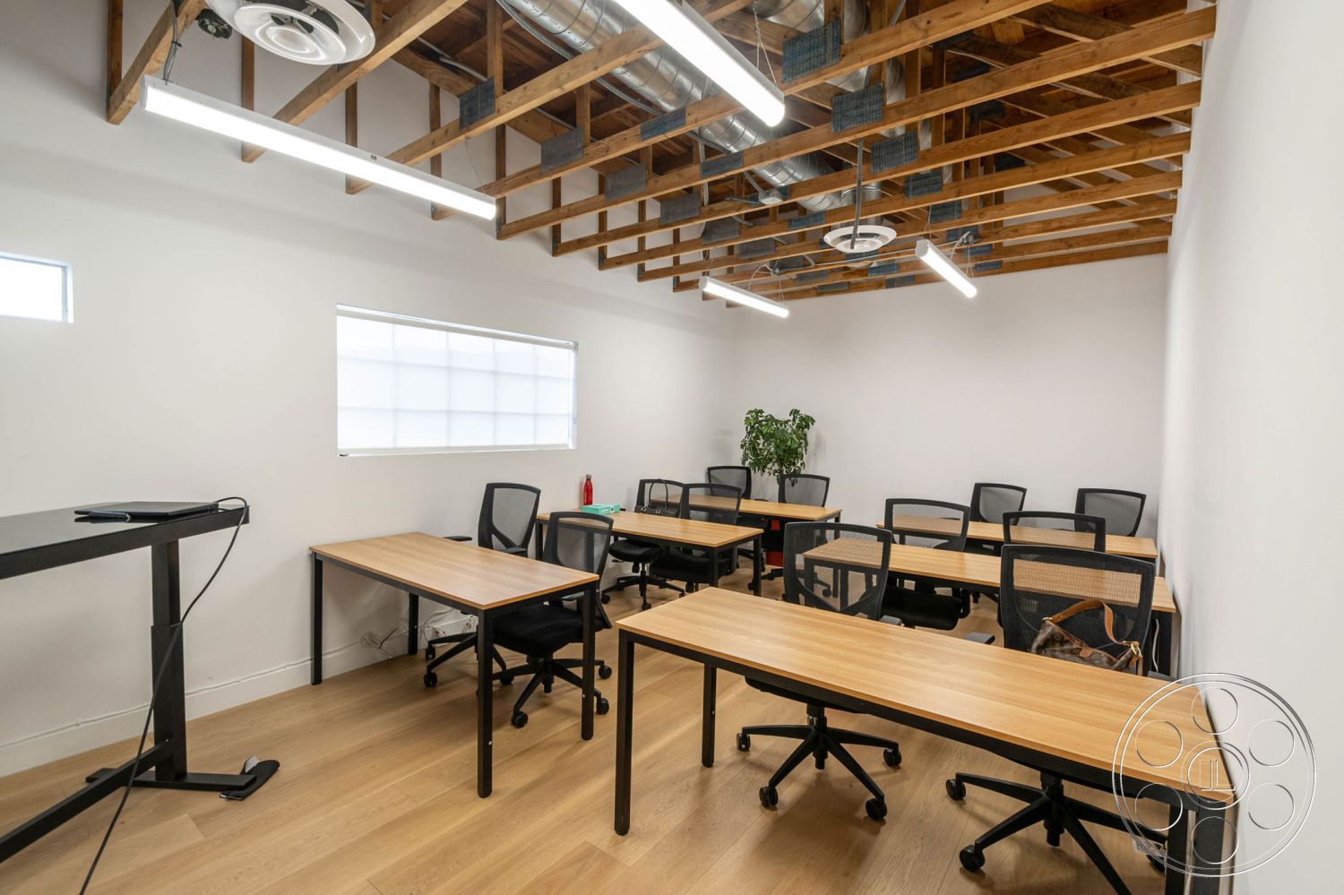 Office 126 - minimalist design, light wood flooring, white painted walls, open ceiling with exposed wooden beam structure, modern style classroom, black metal desk legs with wooden tabletop, task chairs with mesh backs, fluorescent light fixtures, large window with frosted glass, removable partition for flexible layouts, large potted plant for greenery, acoustic ceiling panels for sound absorption