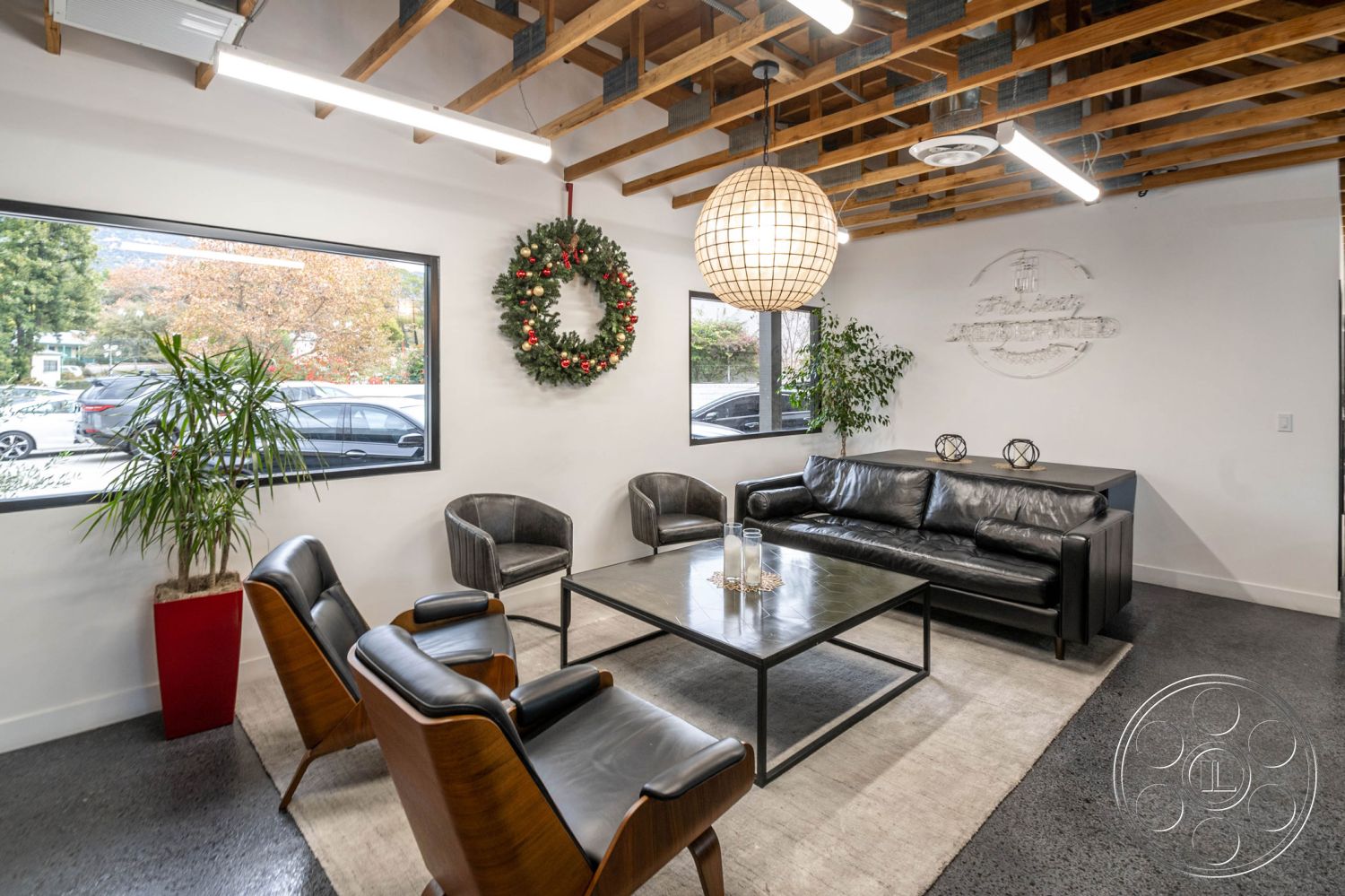 Office 126 - neutral color palette, large windows, wooden accents, concrete floor, minimalist design elements, modern pendant lighting, interior space, seating area, urban setting, green indoor plants, textured plaster walls, metal coffee table, black leather sofa, exposed wood ceiling beams, open layout design, natural light flooding in, decorative holiday wreath, industrial style furnishings, contemporary interior decor