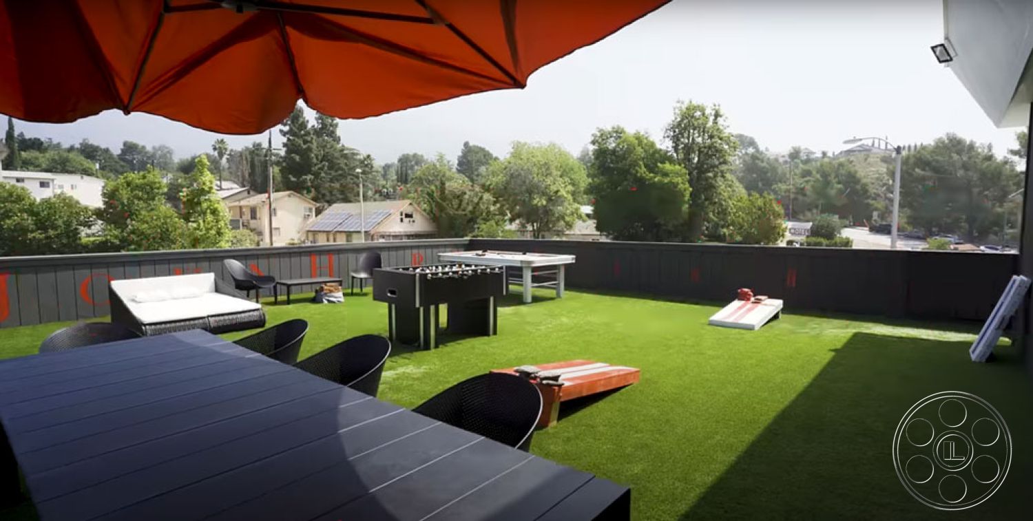 Office 126 - patio, outdoor recreational space, open-air lounge area, artificial turf patio flooring, rectangular outdoor dining table, black metal outdoor chairs, orange patio umbrella, scenic urban rooftop setting, modern outdoor entertainment area, foosball table patio, landscape view with greenery, lawn-style grass surface, exterior balcony space