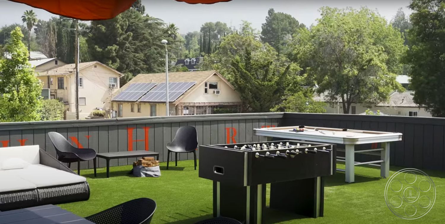 Office 126 - patio, city skyline view, contemporary outdoor furniture, greenery backdrop, landscaped vegetation, urban rooftop setting, modern lounge seating area, artificial grass outdoor floor, wooden deck railing, black foosball table, rectangular outdoor table, exterior wall with painted wood paneling, suburban rooftop patio, outdoor game area, large orange sunshade, exterior glass door, sunny patio space, relaxed entertainment area, comfortable outdoor seating, open-air recreational space