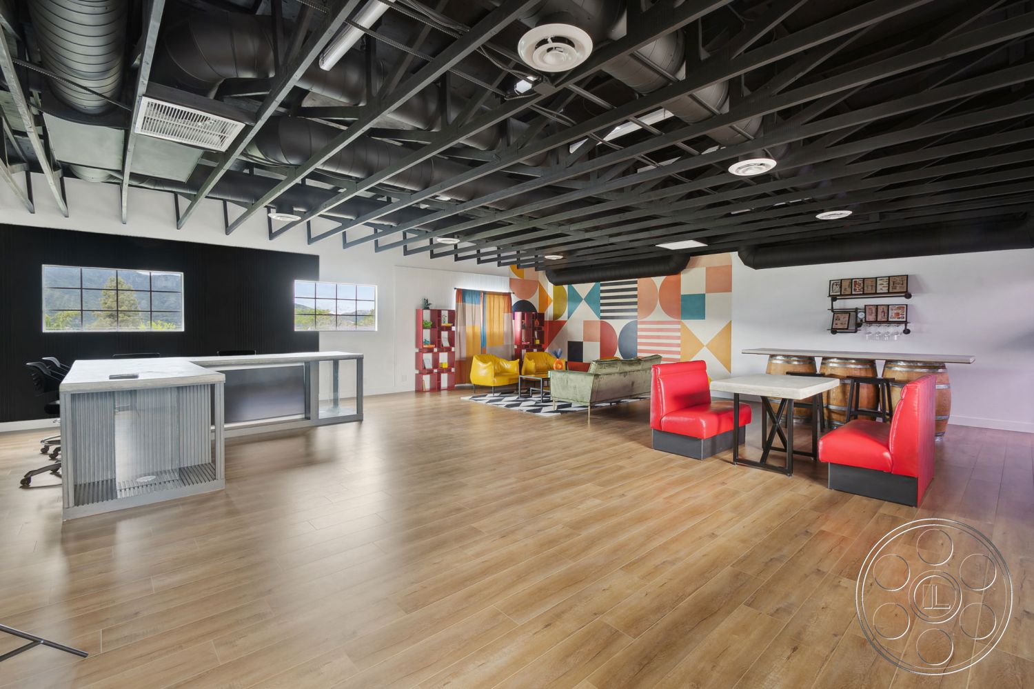 Office 126 - floor-to-ceiling windows, textured wall panels, industrial decor, bright natural lighting, contemporary design elements, black accent wall, laminate wood flooring, modern seating arrangements, functional work area, exposed metal ceiling beams, interior open concept space, glass office desk, multicolored geometric feature wall, red vinyl booth seating, barrel-style table base, casual lounge space, creative workspace setting