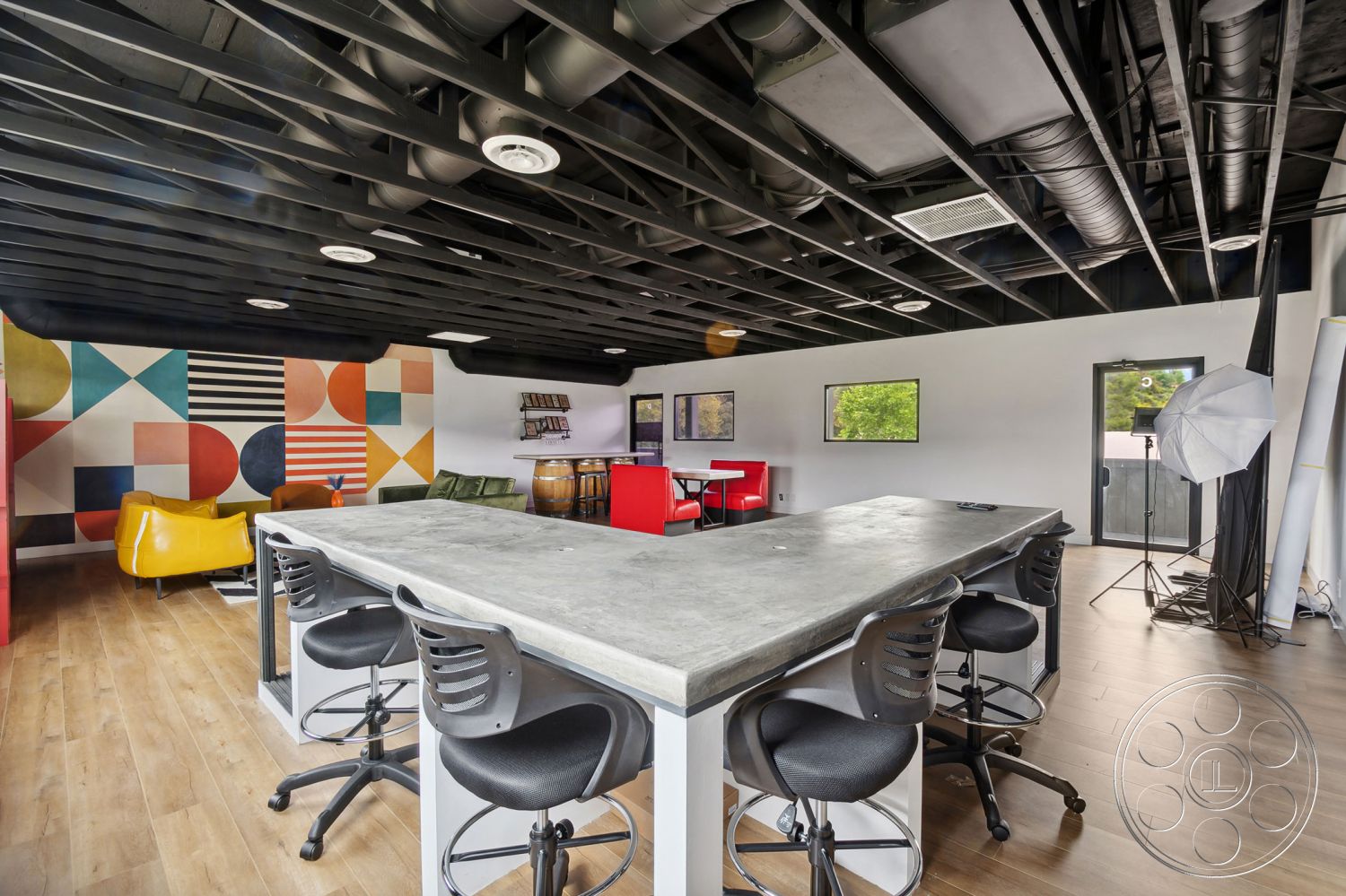 Office 126 - minimalist decor, hardwood flooring, creative workspace, open concept layout, interior space, industrial style, metal bar stools, natural light from windows, casual meeting area, modern dining area, exposed black ceiling beams, concrete countertop bar, colorful geometric accent wall, urban loft setting, functionality focused design, dual-purpose space, entertainment zone