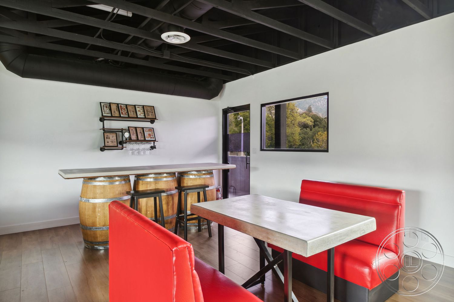 Office 126 - interior hardwood floor, interior white painted walls, interior open floor plan, interior recessed lighting fixtures, interior minimalist design elements, interior concrete table top, interior red vinyl booth seating, exposed black steel ceiling beams, interior concrete bar top, interior wooden barrel stools, interior framed wall art display, interior glass door with black frame, exterior tree line view, interior industrial-style decor