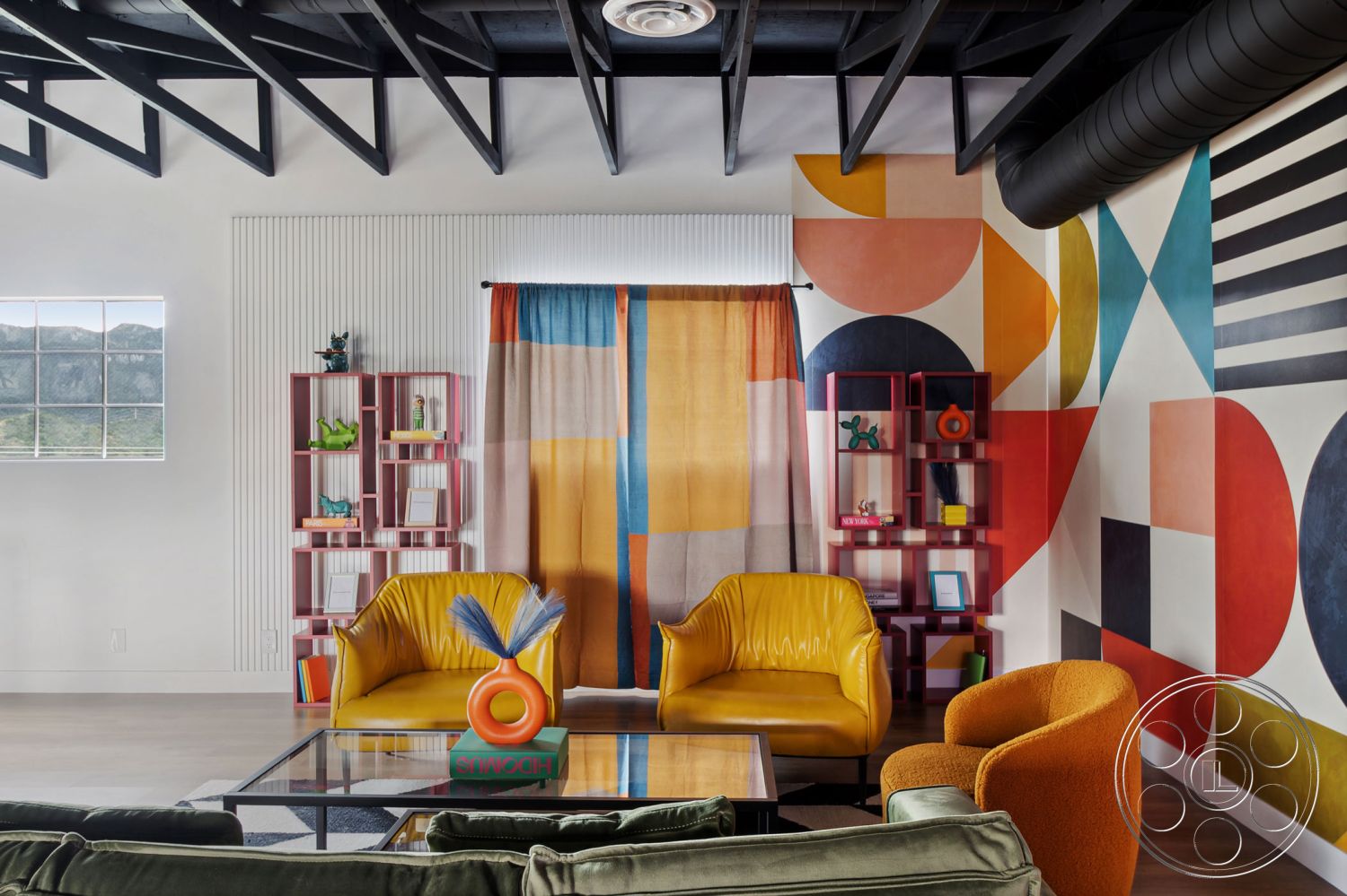 Office 126 - exposed wood ceiling beams interior, white painted walls interior, hardwood living room floors interior, open concept living area interior, colorful geometric mural wall treatment interior, modern glass coffee table interior, yellow leather armchair interior, orange accent chair interior, custom bookshelf with open shelving interior, textured fabric curtains with colorful patterns interior, industrial air duct ceiling feature interior, natural light from large window interior, bright and eclectic interior design, stylish decorative accents and sculptures interior