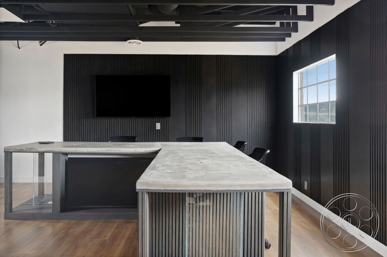 Office 126 - modern minimalist aesthetic, flat-screen TV mounted on wall, white painted walls, wood laminate flooring, contemporary office design, black ergonomic office chairs, exposed black steel ceiling beams, large window with city view, concrete conference table, glass panel base, black ribbed wall treatment