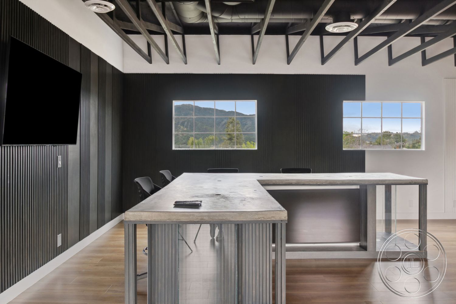 Office 126 - neutral color palette, hardwood flooring, minimalist design, task lighting, open-plan layout, exposed wood ceiling beams, glass partition windows, modern industrial style, concrete conference table, metal ductwork ceiling, stainless steel base, black accent wall with vertical paneling, large square windows with mountain view, seating area with ergonomic chairs