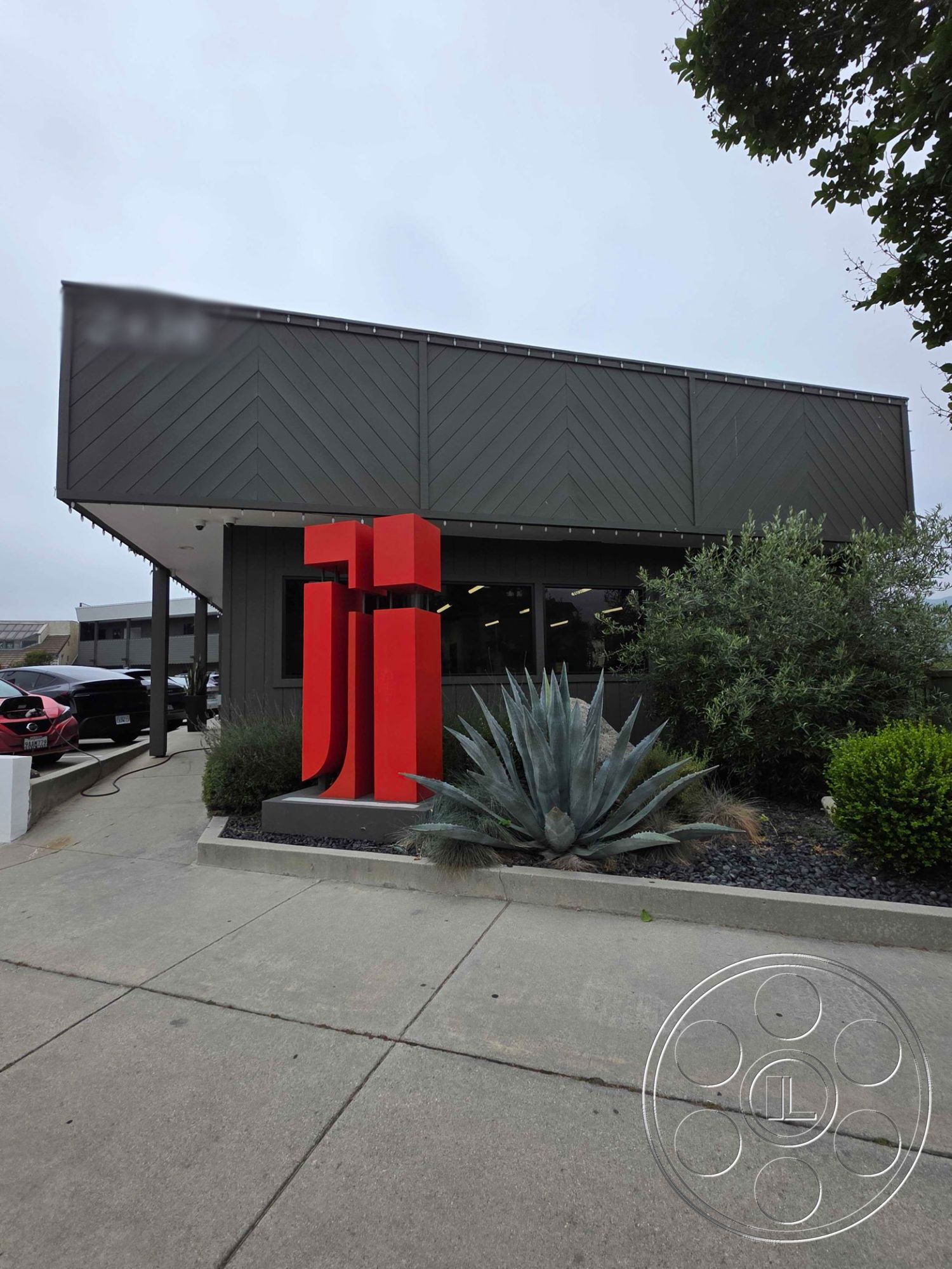 Office 126 - minimalist design, surrounding greenery, modern architectural style, concrete walkway, outdoor lighting fixtures, succulent landscaping, hedge landscaping, sloped metal roof, urban commercial setting, exterior black wood paneling, red metal sculpture, stone garden bed, glass front windows, gray concrete surface, asphalt parking area, modern entrance design
