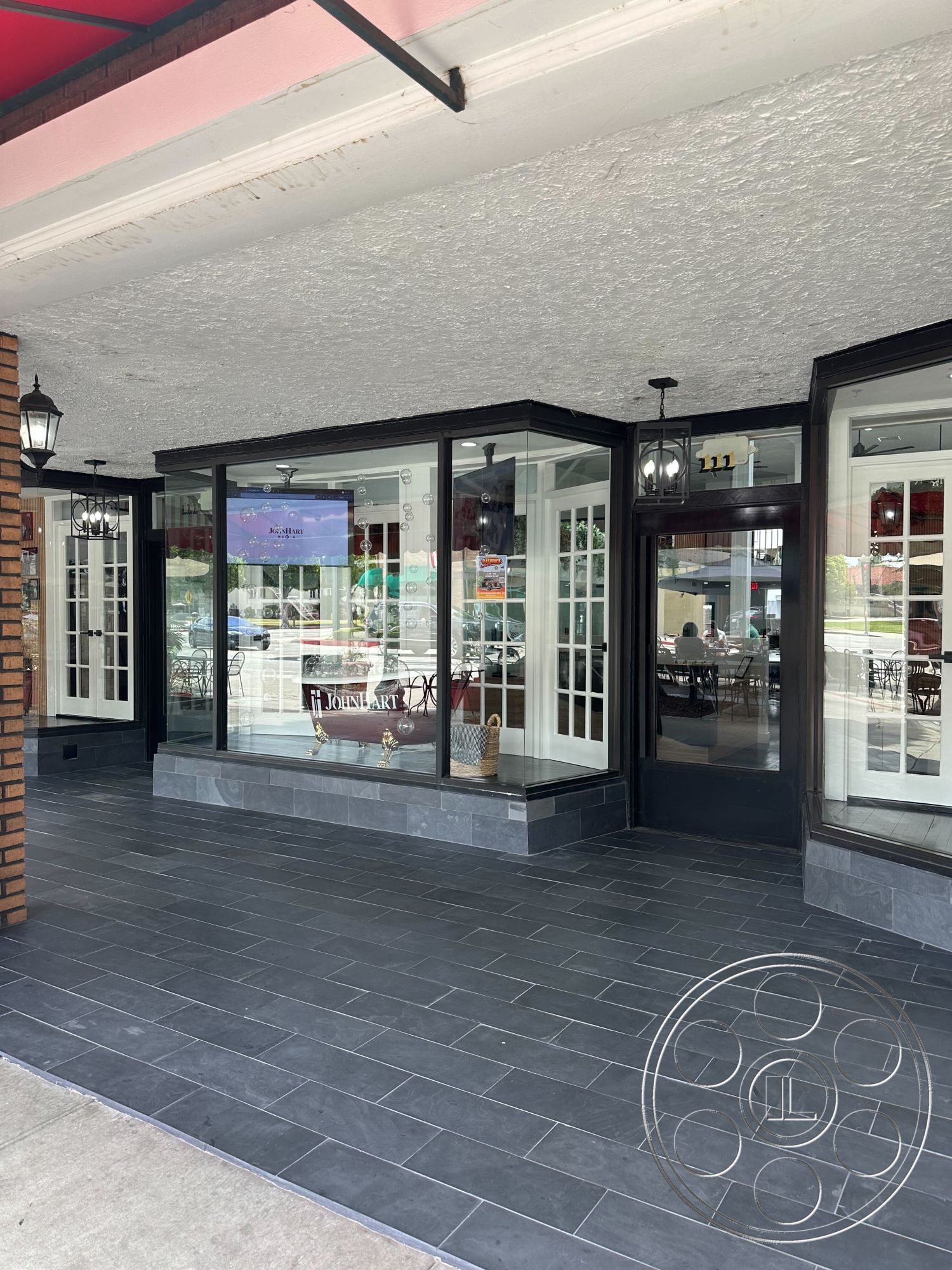 Office 127 - exterior, outdoor seating area, urban setting, exposed brick wall, textured plaster ceiling, black frame windows, glass storefront windows, black slate tile flooring, white paneled doors, vintage-style outdoor lanterns, commercial storefront design