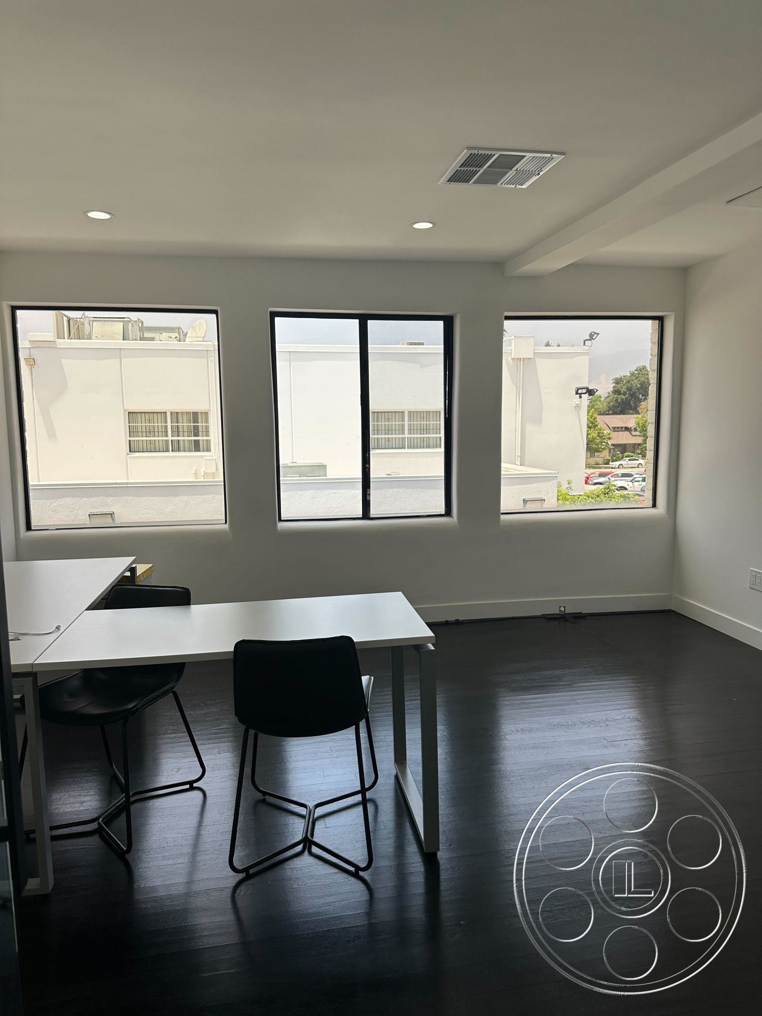 Office 127 - minimalist design, open floor plan, bright natural light, urban setting, functional workspace, floor-to-ceiling windows, dark hardwood flooring, black accent chairs, recessed lighting fixtures, white painted walls, modern desk with metal legs, rectangular room layout