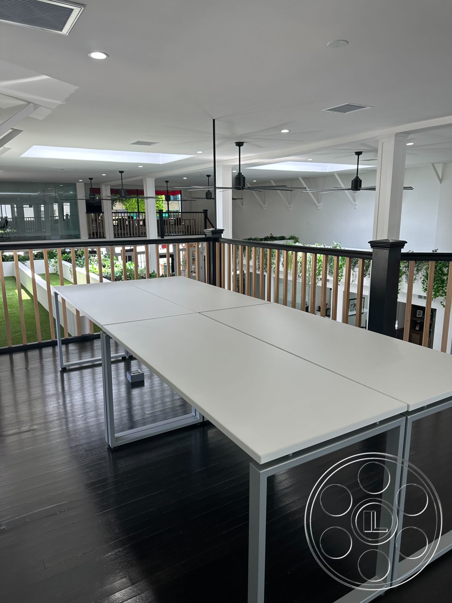 Office 127 - high ceilings, neutral color palette, minimalist design, green plant accents, communal gathering area, exposed ceiling beams, black hardwood flooring, natural light from skylights, open-concept interior, glass railing balcony, recessed LED lighting, metal table legs, modern industrial style, modern white conference table, multi-functional workspace, city view from balcony