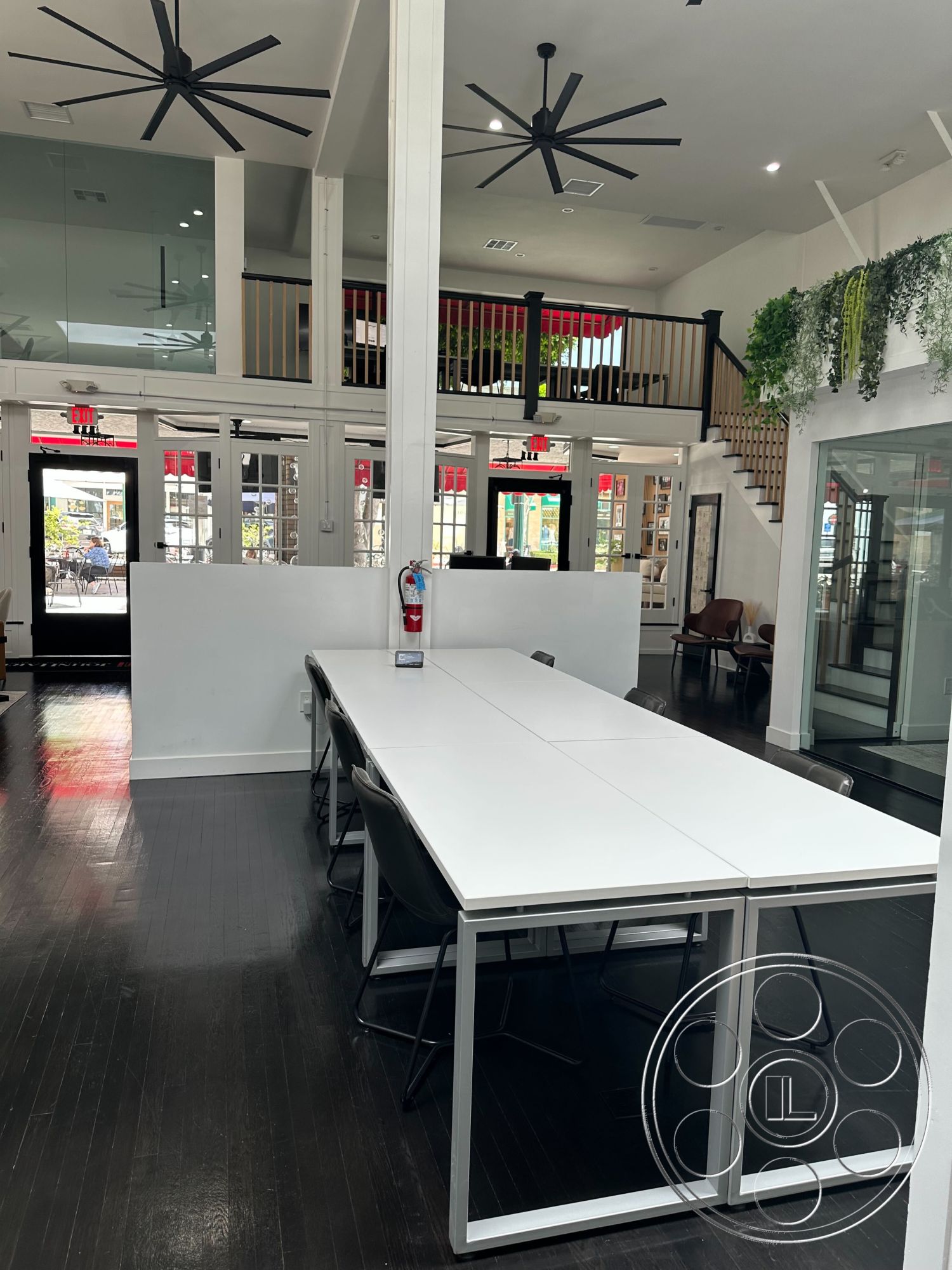 Office 127 - white walls, large windows, natural light, hardwood flooring, open floor plan, urban setting, suspended lighting fixtures, exposed ceiling beams, modern staircase, black dining chairs, ceiling fans, glass partition walls, flexible meeting space, contemporary table design, glass door entry, bamboo plant decor