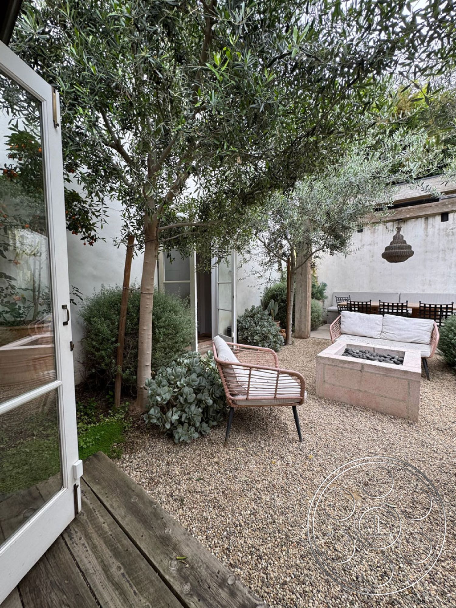 Spanish 165 - decorative plants, outdoor living space, landscape greenery, modern lounge chairs, concrete fire pit, wood deck flooring, minimalist outdoor design, glass door entry, gravel patio ground, tall tree canopy, stucco exterior wall, cozy garden setting, exposed beam details, rustic outdoor furniture, relaxed backyard ambiance