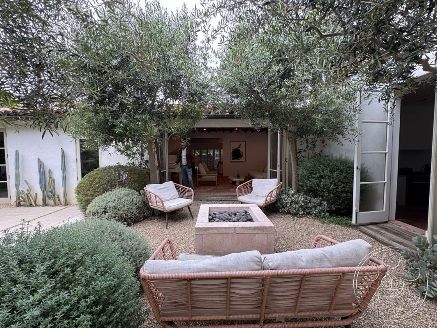 Spanish 165 - natural stone accents, gravel landscaping, seamless indoor-outdoor flow, modern fire pit, olive trees, mid-century modern style, exposed wood ceiling beams, lush green shrubbery, urban garden setting, exterior patio area, glass door entrance, outdoor leisure space, stone fire pit base, rattan outdoor seating, decorative cactus wall art, interior living area view, earth tone color palette, courtyard design