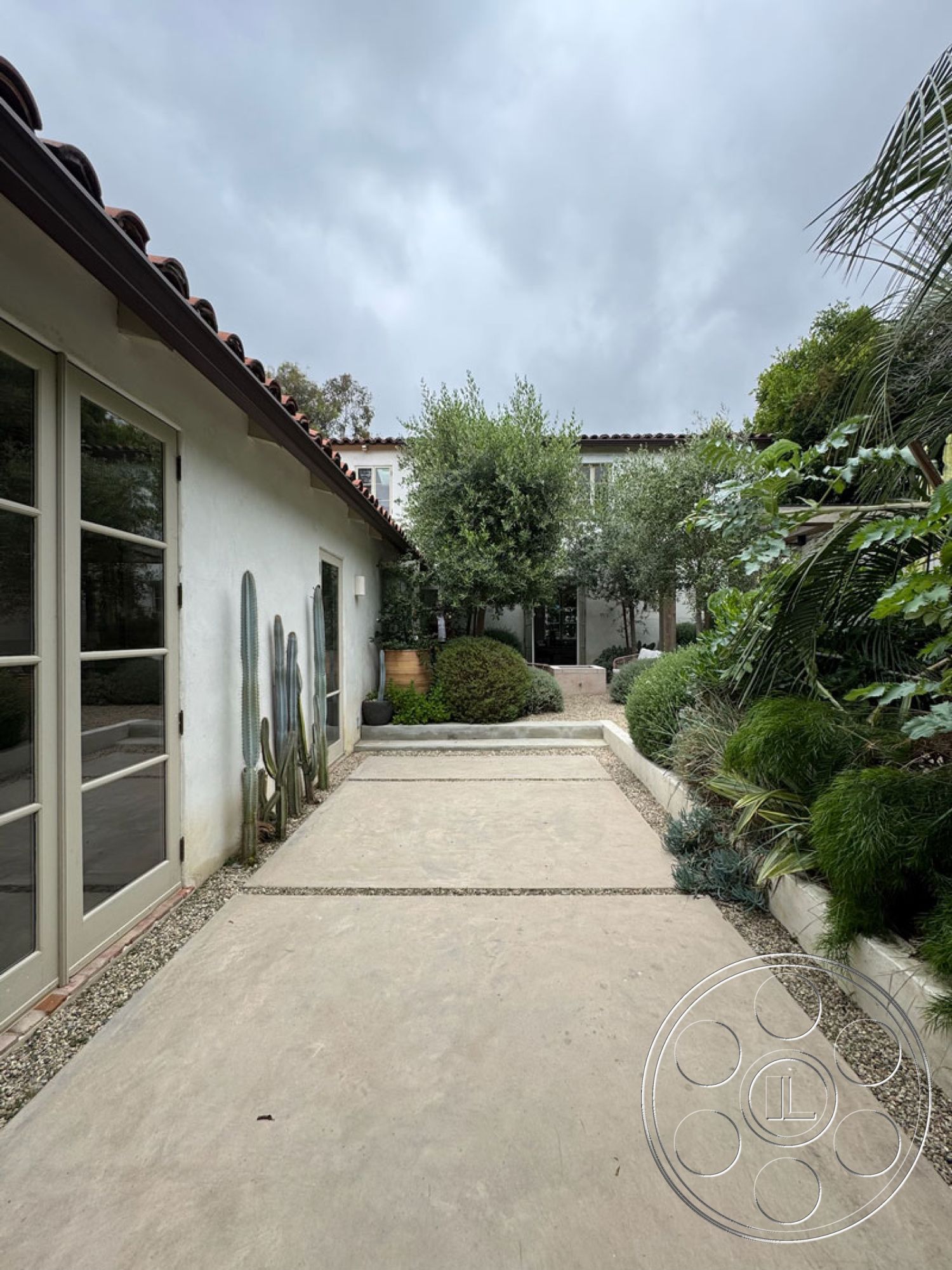 Spanish 165 - exterior glass door, exterior concrete pathway, exterior textured plaster walls, exterior wood beam entryway, outdoor desert landscaping, exterior potted plants, horizontal concrete slabs, exterior gravel accents