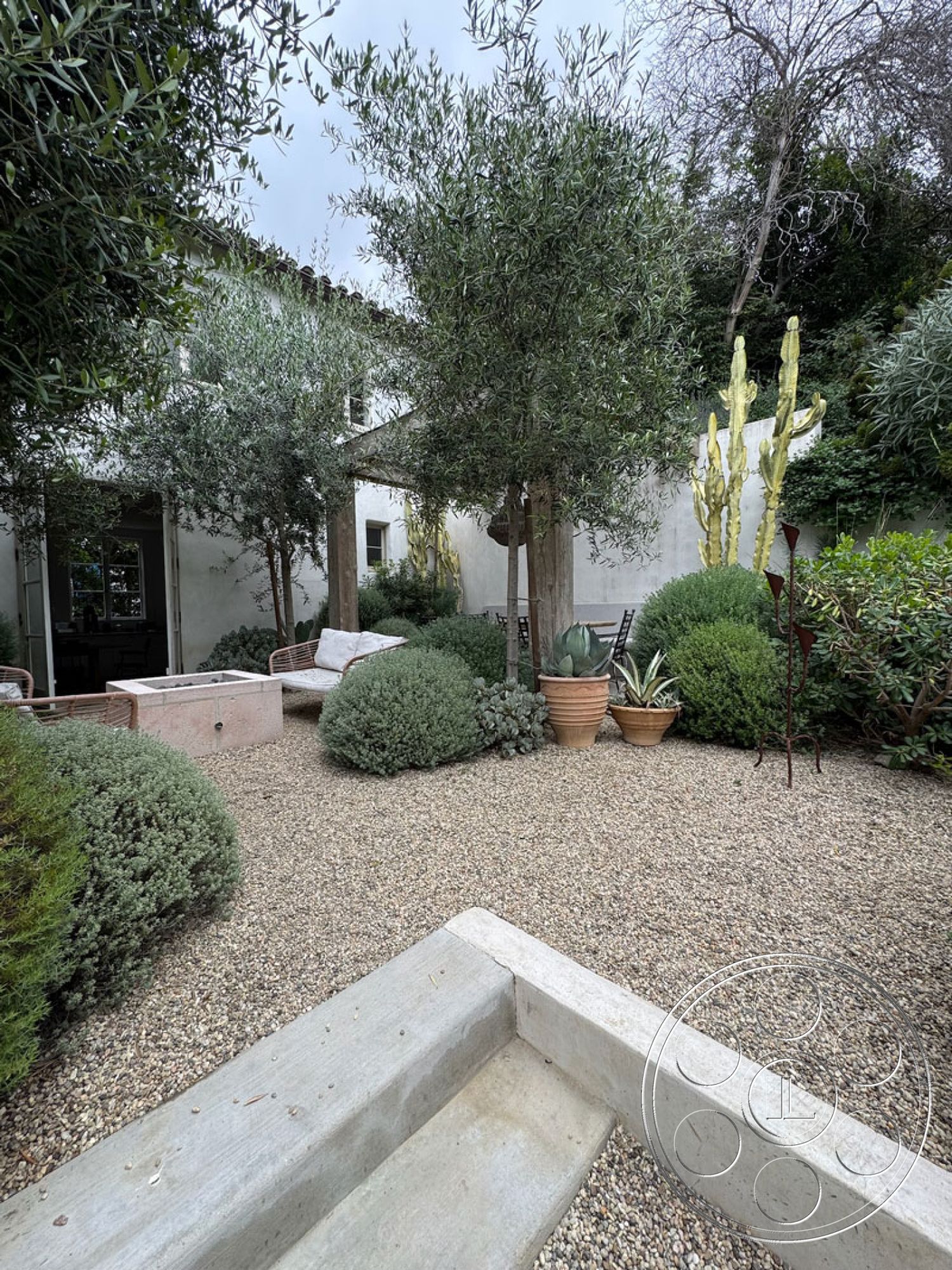 Spanish 165 - exterior gravel landscaping, exterior concrete patio border, exterior potted succulents, exterior olive trees, exterior stone fire pit, exterior wood beam pergola, exterior minimalistic seating area, exterior desert-inspired garden, exterior native plants, exterior textured stucco walls, exterior modern garden sculptures, exterior shaded relaxation space