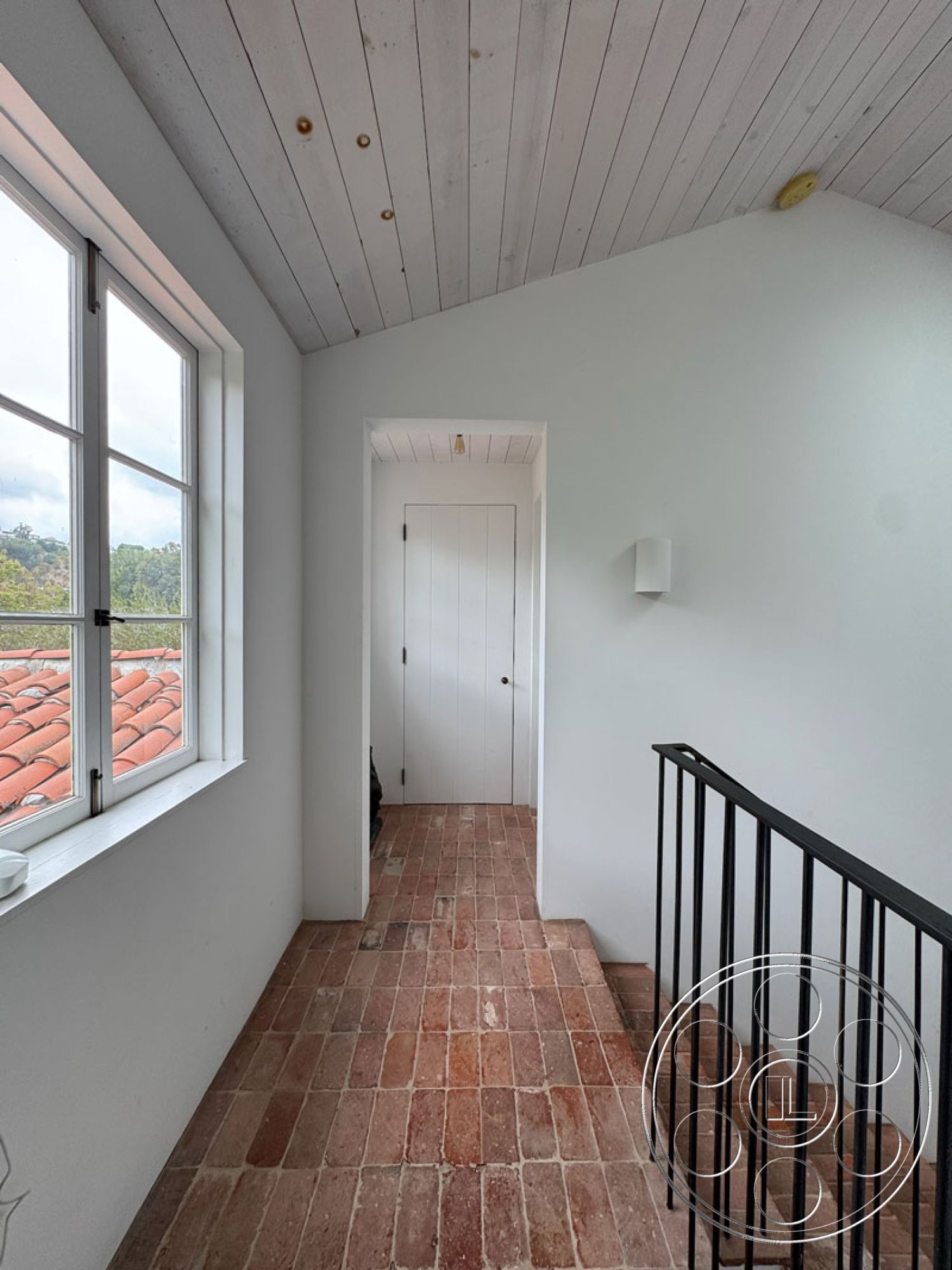 Spanish 165 - neutral color palette, vaulted ceiling, modern farmhouse aesthetic, interior hallway, natural light interior, white painted walls, large casement windows, wood plank ceiling, exposed brick flooring, black metal stair railing, rectangular hallway, traditional door design