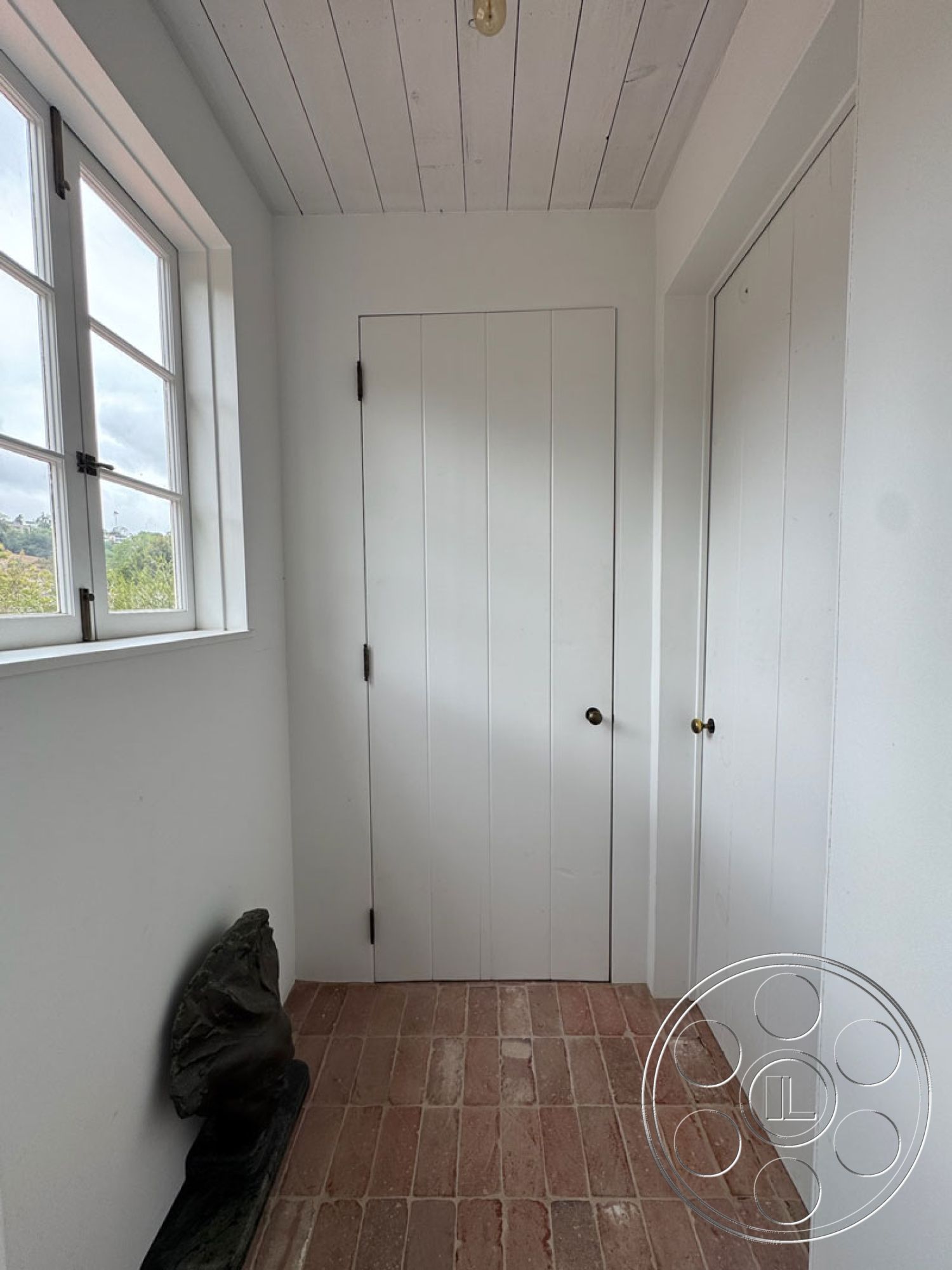 Spanish 165 - clean lines, minimalist design, bright natural light, open space layout, white painted walls, interior entryway, exposed brick flooring, white wood plank ceiling, panel door, door hardware with brass knob, natural stone sculpture