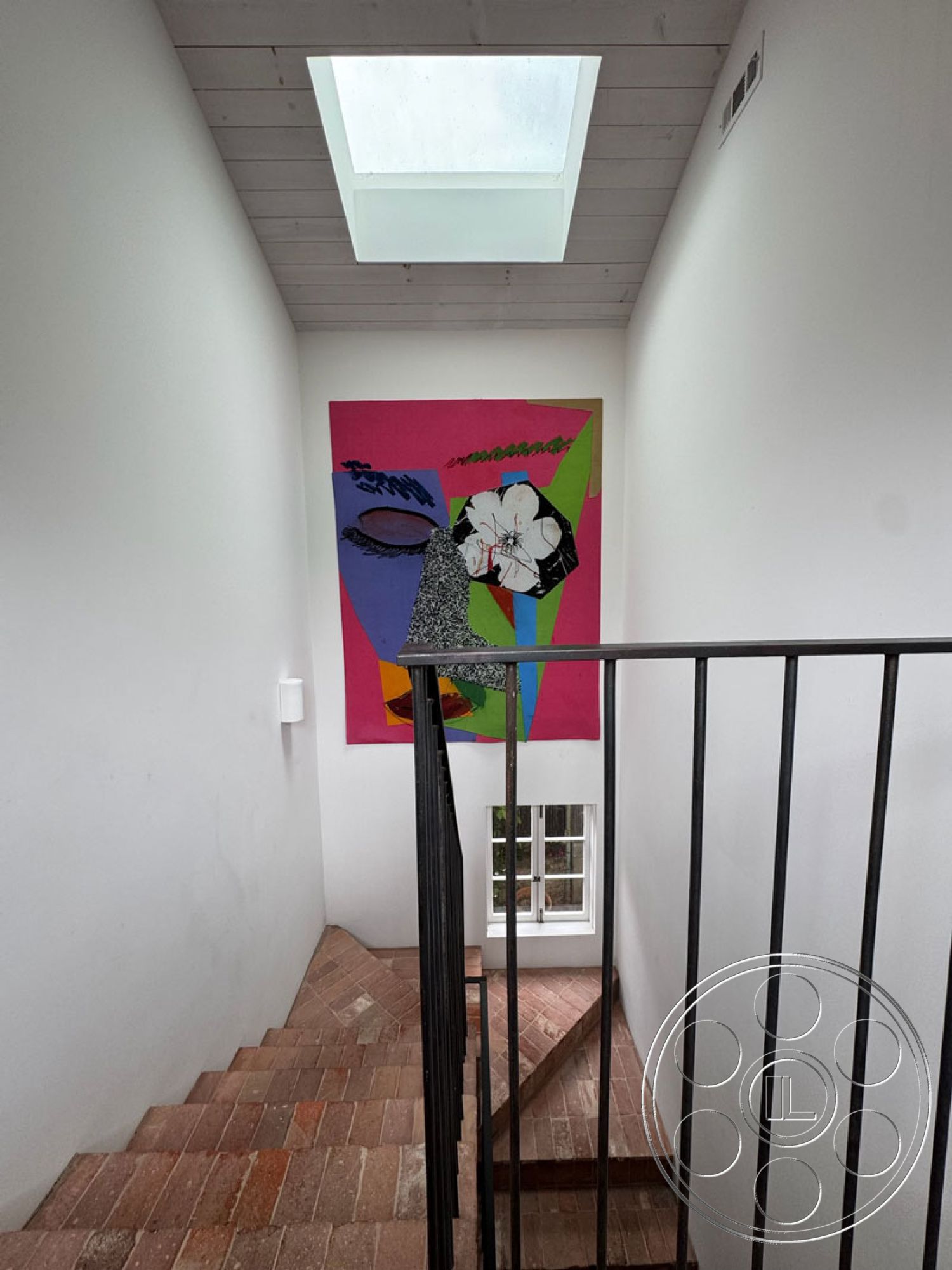 Spanish 165 - minimalist aesthetic, wood ceiling beams, natural light from skylight, white painted walls, modern architectural design, exposed brick stair flooring, black metal stair railings, skylight ceiling feature, colorful abstract wall art, interior staircase, functional corridor space, brick step details