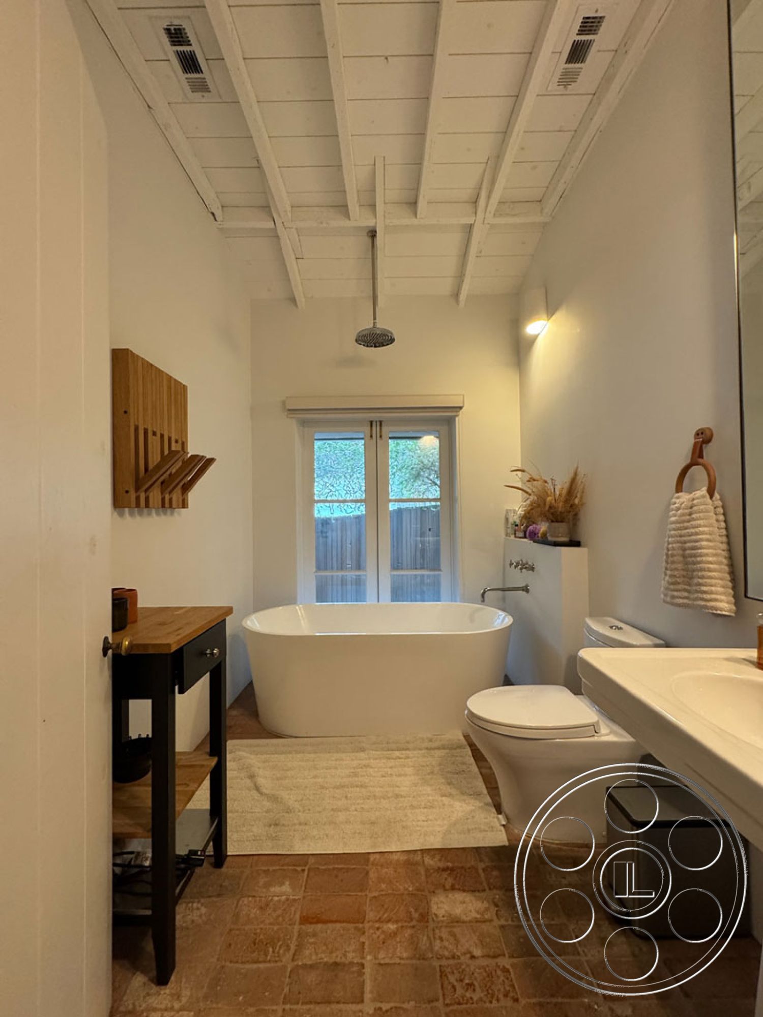 Spanish 165 - freestanding soaking tub, interior bathroom with terracotta tile flooring, white shiplap ceiling with exposed beams, modern wall-mounted bathroom sink, dark wood storage cabinet, large mirror with minimalist frame, sliding glass patio doors, textured white wall finish, soft area rug in neutral tones, contemporary chrome showerhead, natural light from outdoor view, decorative bathroom accessories, minimalist towel rack, clean and bright bathroom space