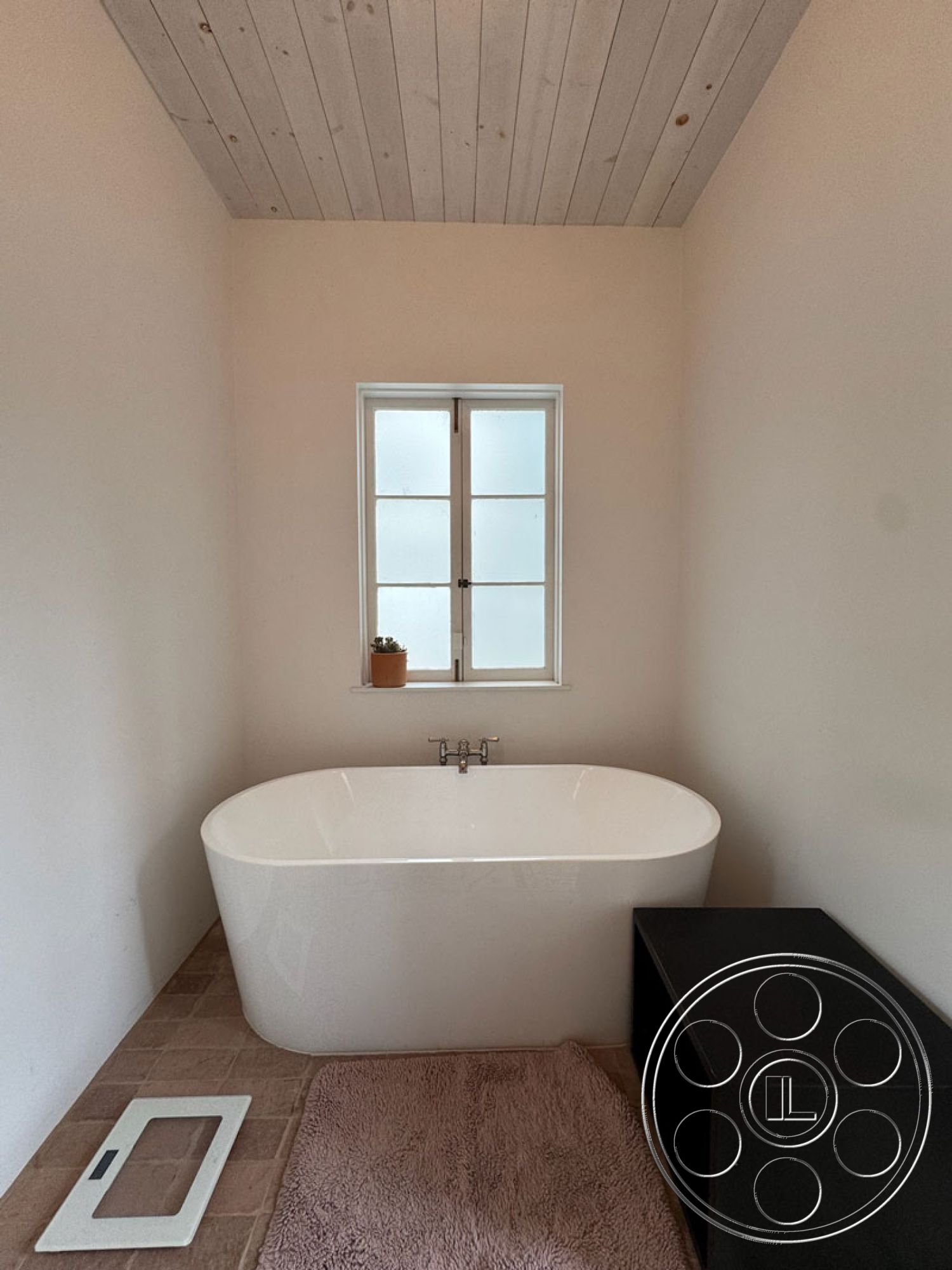 Spanish 165 - natural light from window interior, white painted walls interior, planked wood ceiling interior, freestanding soaking tub interior, tile bathroom flooring interior, frosted glass window interior, black storage cabinet interior, textured bath mat interior