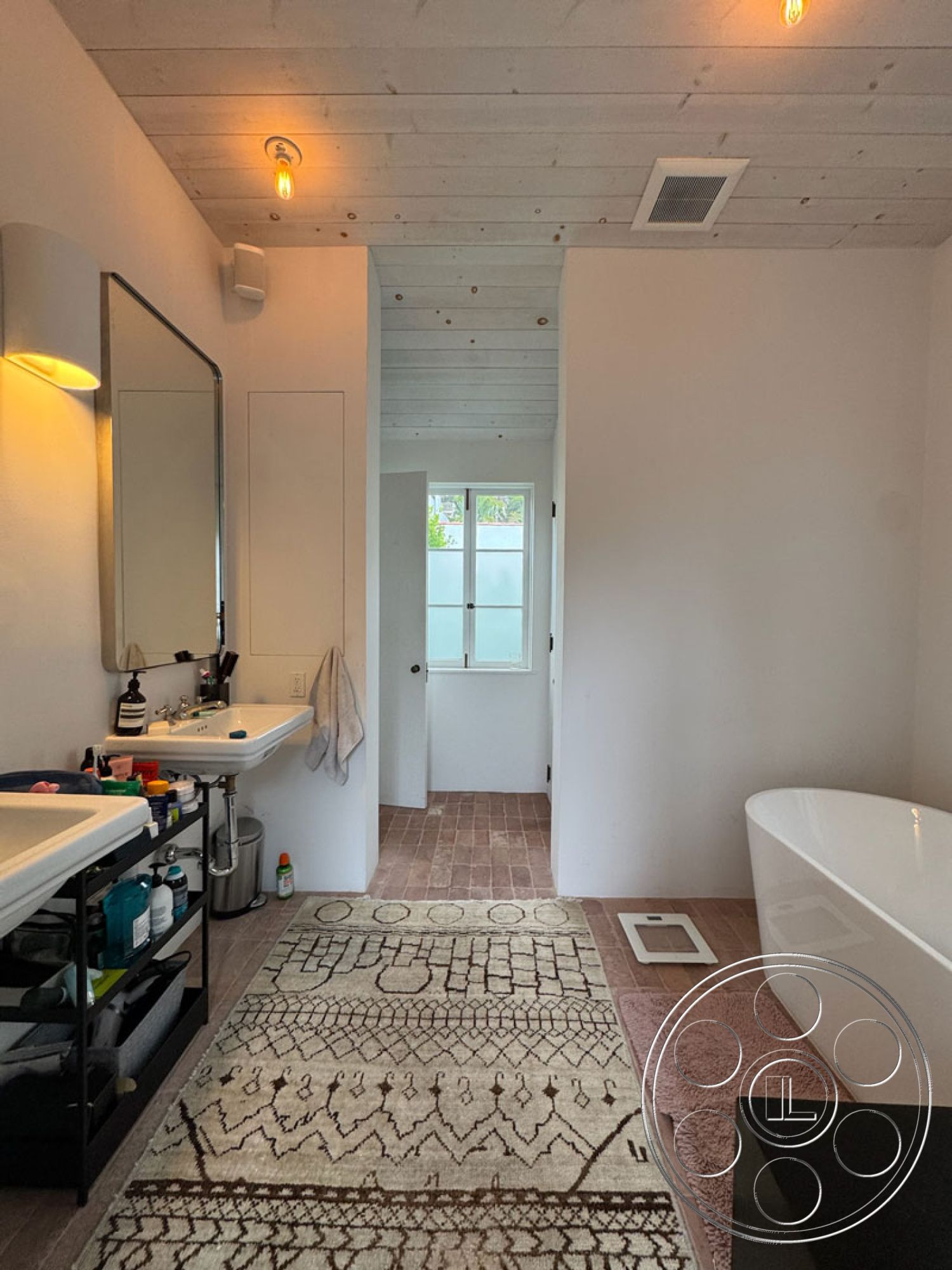 Spanish 165 - minimalist decor, neutral color palette, natural light, open floor plan, freestanding bathtub, woven area rug, terracotta tile flooring, stylish storage solutions, exposed wood ceiling beams, interior bathroom, white painted walls, modern bathroom vanity, mirrored wall sconce lighting, glass door with window