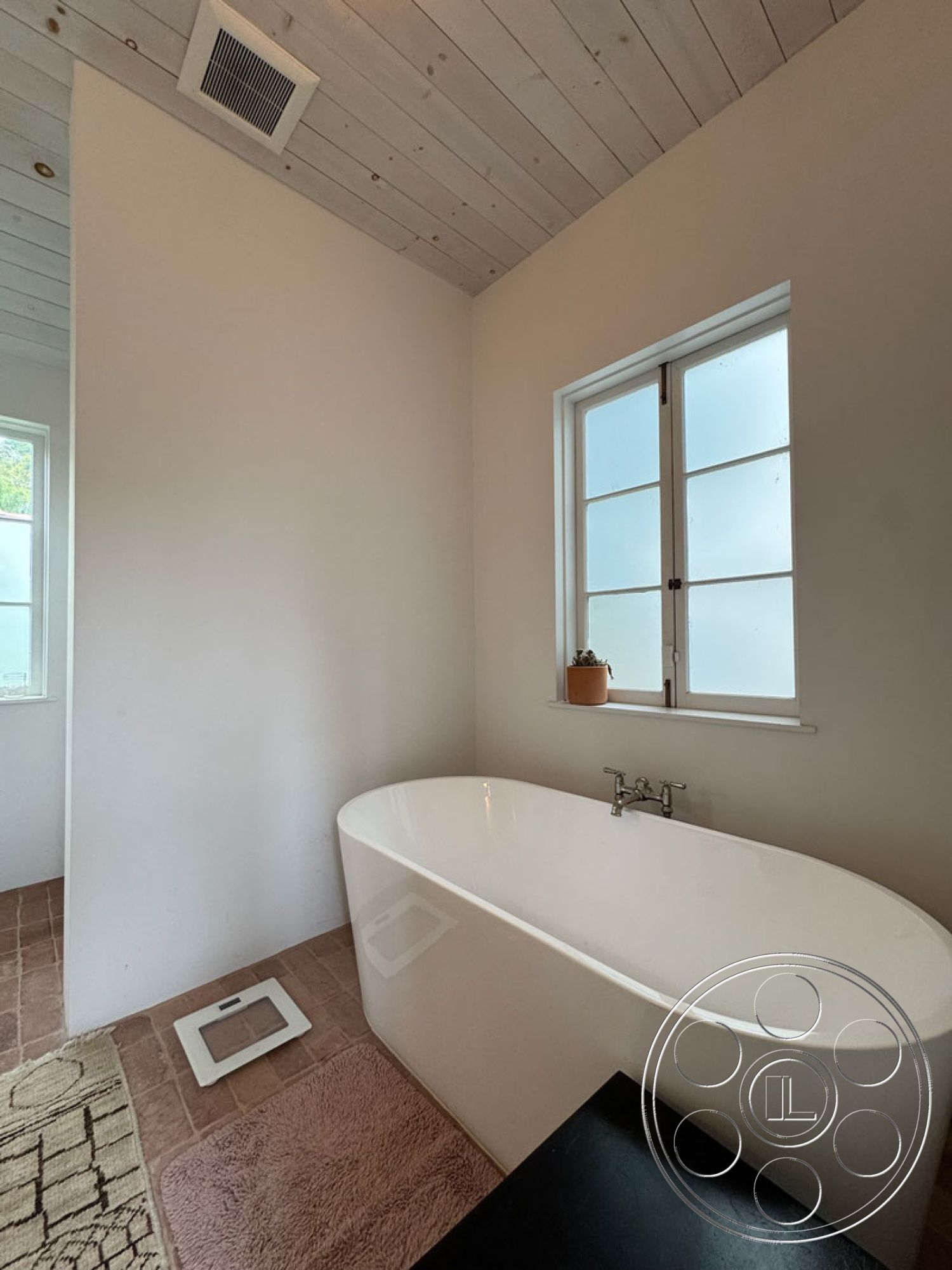 Spanish 165 - minimalist decor, neutral color palette, natural light, stone tile flooring, interior bathroom, textured bath mat, white painted walls, freestanding soaking tub, modern faucet fixtures, wood plank ceiling, large window with grid design, potted plant accent, open and airy space