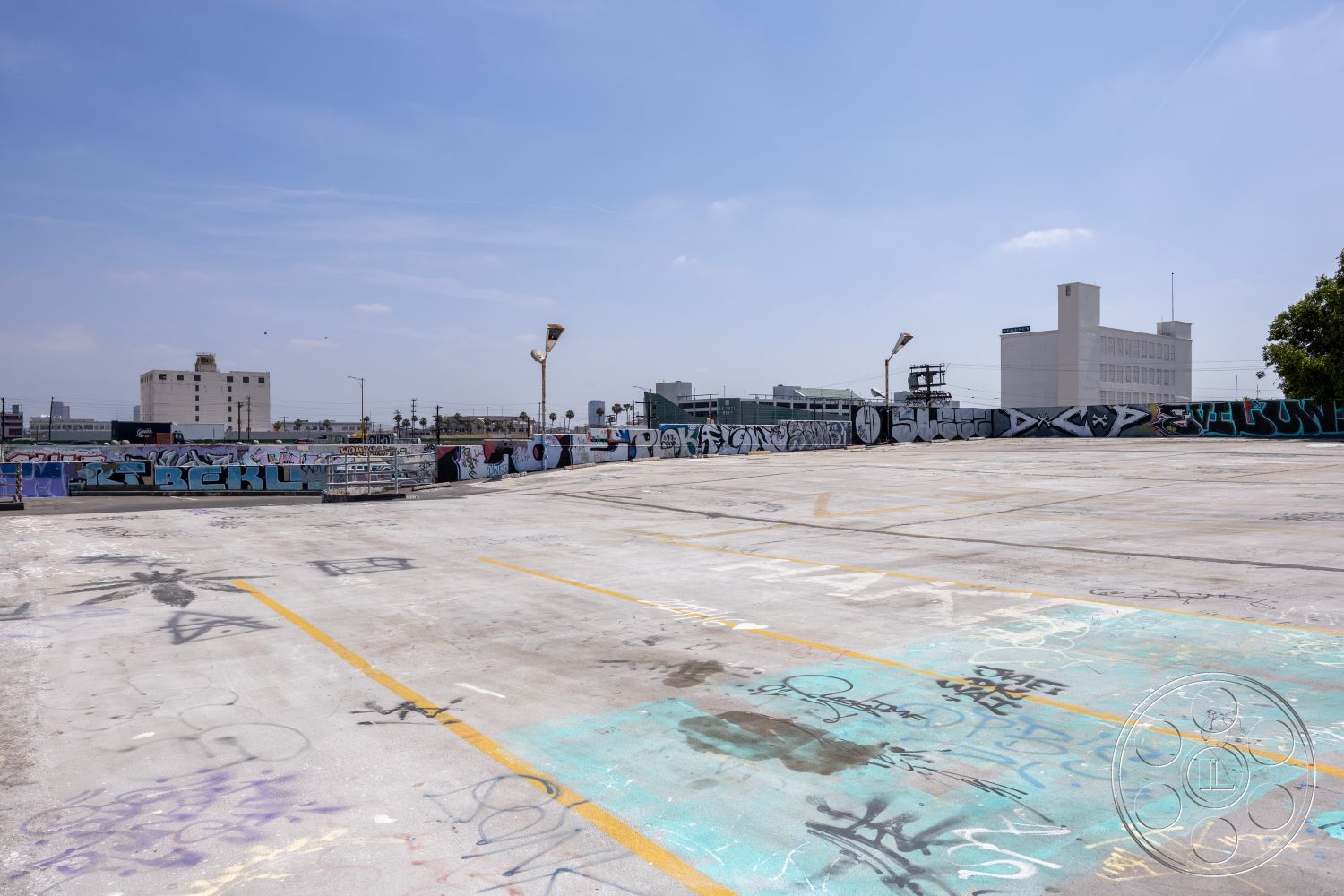 Rooftop 51 - urban landscape, open-air space, city skyline view, graffiti wall art, overhead lighting fixtures, modern industrial design, urban rooftop setting, concrete parking deck, exposed concrete surface, industrial urban environment, brightly painted concrete floor, parking lot stripes, flat rooftop structure, concrete barriers