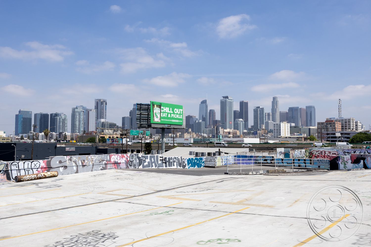 Rooftop 51 - city skyline view, graffiti wall art, flat roof structure, industrial style architecture, concrete parking deck, urban rooftop space, steel railing details, exposed concrete finish, outdoor urban environment, mixed-use building context, city background, graffiti-covered surfaces, suburban urban fringe, open-air rooftop, commercial district setting