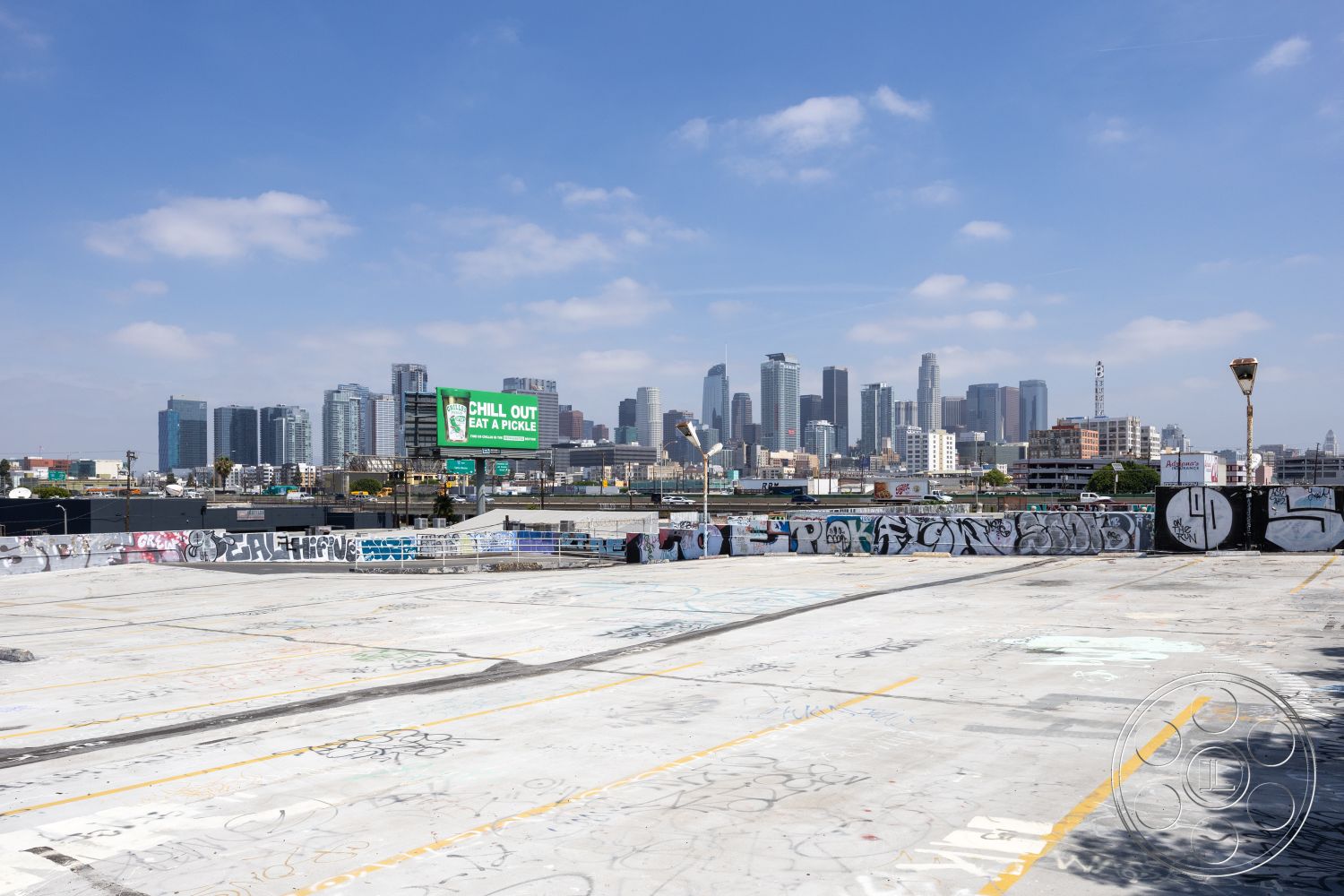 Rooftop 51 - open-air space, urban skyline view, hardscape design, metal light fixtures, graffiti wall art, exterior concrete rooftop, commercial parking lot, flat concrete surface, industrial cityscape, vacant urban space, suburban skyline backdrop, unknown signage, mixed-use urban setting, city backdrop, paved rooftop, concrete lot with street art