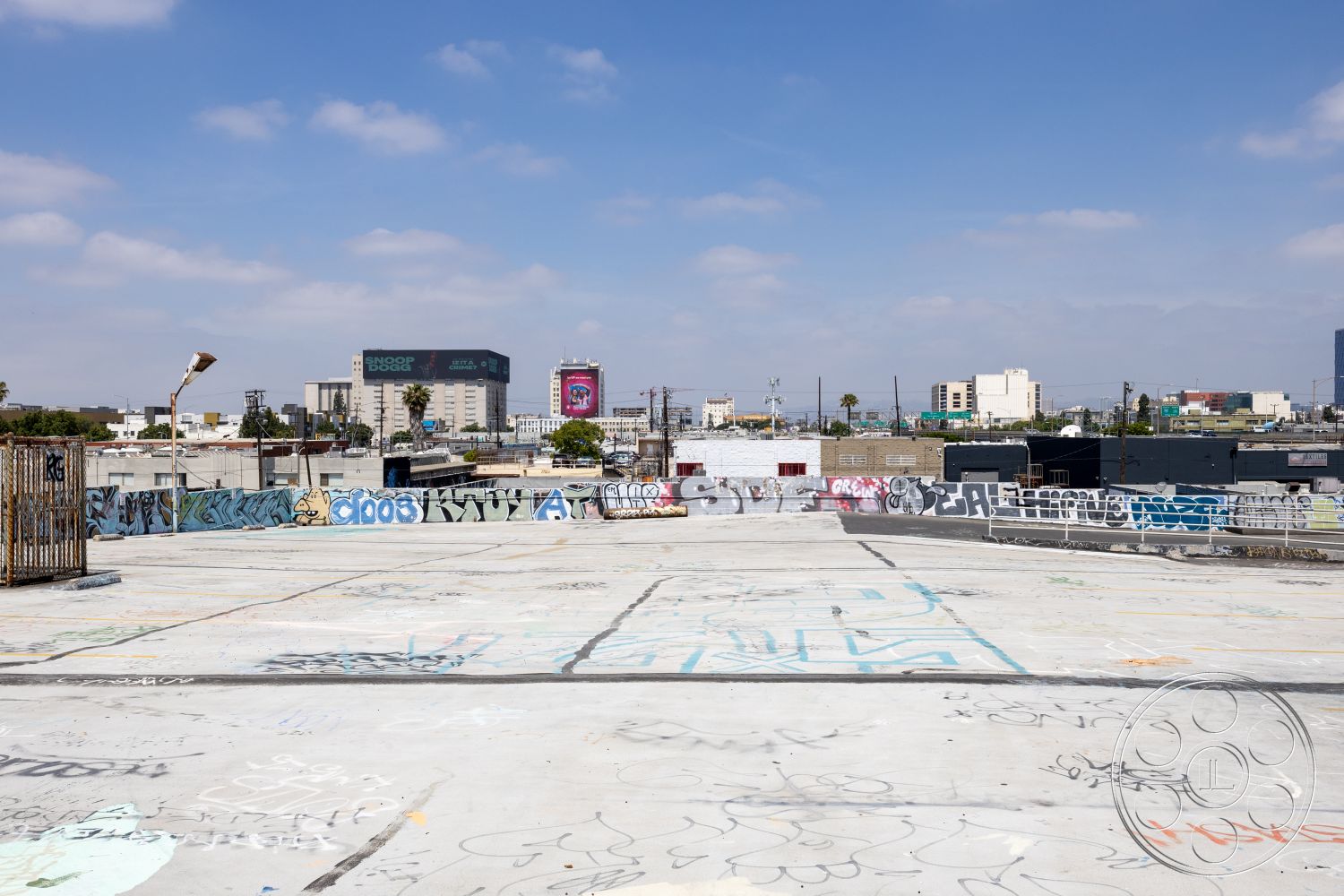 Rooftop 51 - urban skyline view, graffiti wall art, surrounding palm trees, industrial setting, exterior concrete rooftop, commercial building surroundings, flat rooftop surface, fence railing detail, city building backdrop, open-air urban space, paved concrete floor, metal utility pole