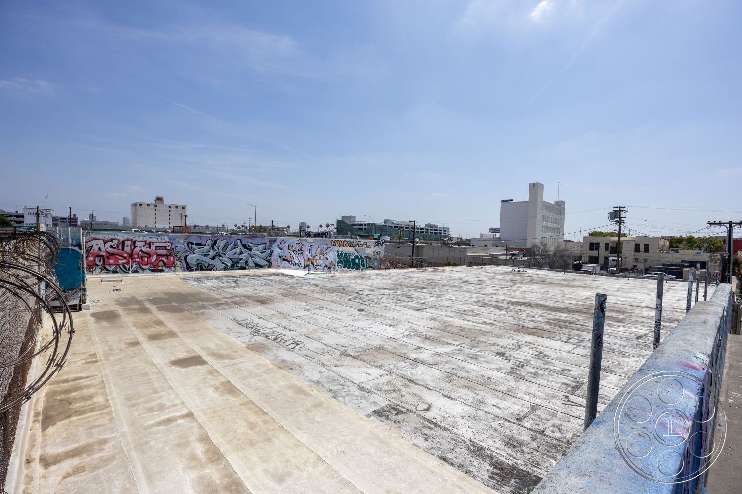 Rooftop 51 - graffiti wall art, surrounding city skyline view, exposed concrete rooftop, flat rooftop surface, industrial urban setting, barbed wire fence details, utility poles and overhead wires, concrete slab foundation, sunny blue sky environment, unfinished exterior space