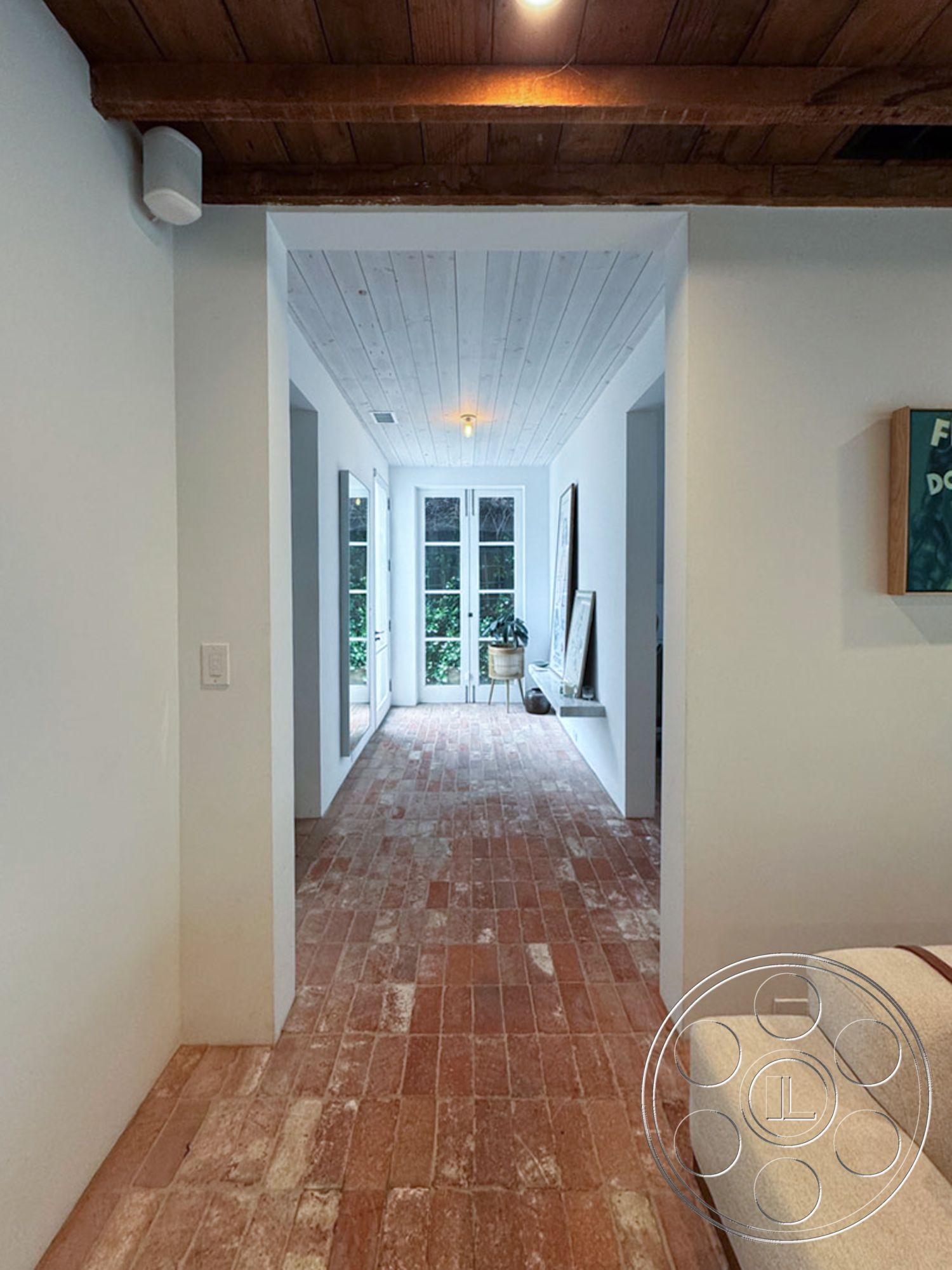 Spanish 165 - neutral color palette, open floor plan, decorative wall art, arched doorways, rustic decor elements, textured wood ceiling, exposed wood ceiling beams, minimalist interior design, white painted walls, natural light-filled interior, brick hallway flooring, French door entrance, garden view from interior, smooth transition from hallway to patio, high ceiling entryway, tranquil indoor environment