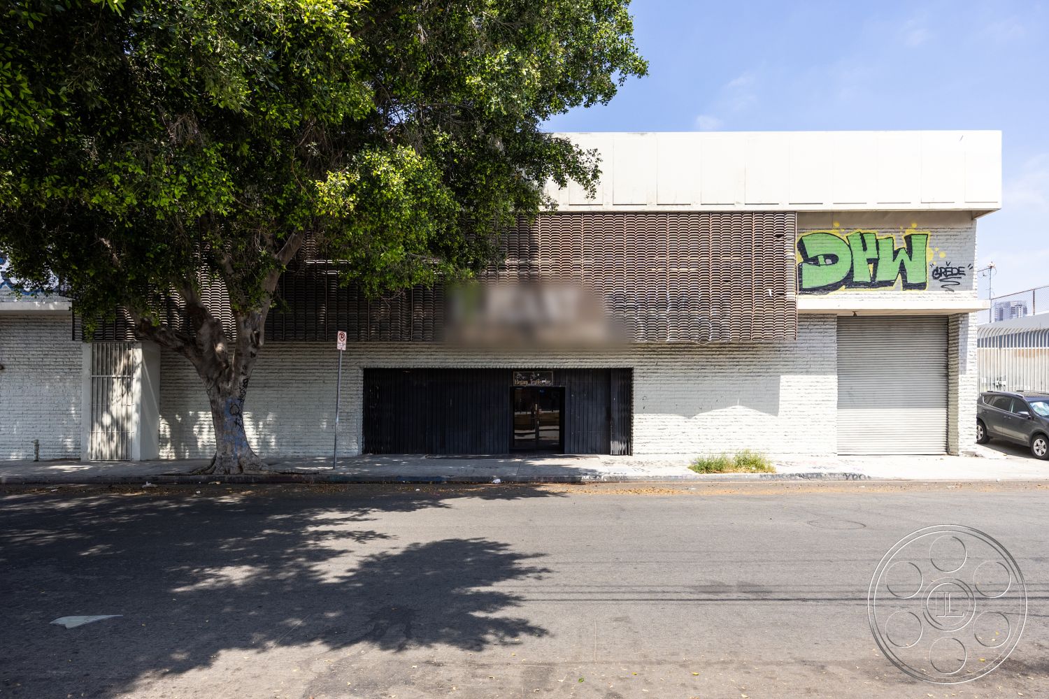 Warehouse 61 - flat roofing, minimalist exterior design, surrounding urban environment, industrial style architecture, exposed brick wall exterior, urban street setting, metal slatted facade, concrete commercial building, entryway with black wooden doors, leaded glass window details, green graffiti art, large shade tree in front, asphalt street surface