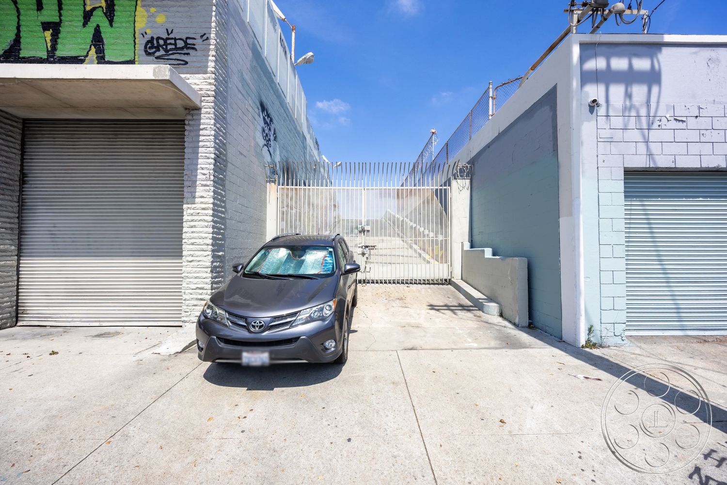 Warehouse 61 - minimalist design elements, urban setting, exposed brick wall, industrial aesthetic, graffiti wall art, roll-up garage door, flat roof design, industrial-style architecture, concrete parking surface, metal security gate, city backdrop, street-level access, gray painted concrete wall, commercial exterior, modern building facade, concrete block construction, steel fence enclosure, straight driveway, hard surface driveway, functional exterior space