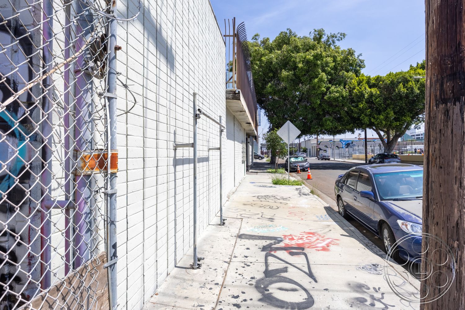 Warehouse 61 - concrete pavement, urban setting, outdoor signage, chain link fence, graffiti wall art, exterior concrete block walls, exterior white painted brick, urban sidewalk paving, exterior landscaping with trees, adjacent street view, industrial perimeter fencing, urban street environment
