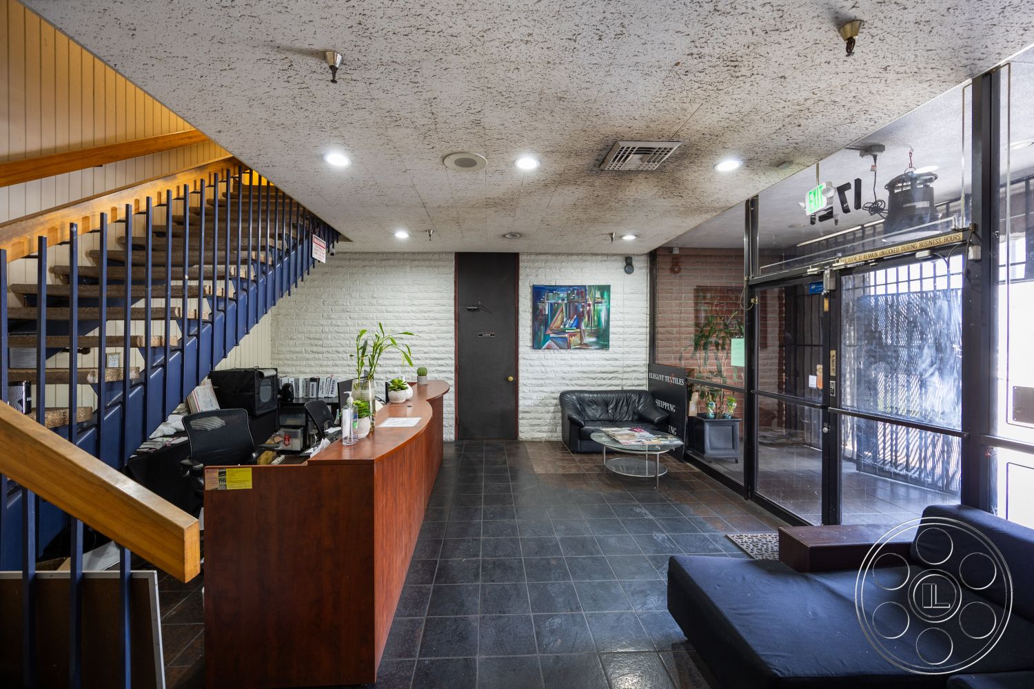 Warehouse 61 - exposed concrete walls interior, open layout interior, industrial style architecture interior, textured ceiling finish interior, dark tiled floor interior, wooden staircase with metal railings interior, reception desk made of stained wood interior, glass entry doors interior, modern black leather seating area interior, artwork on wall interior, indoor plant accent interior