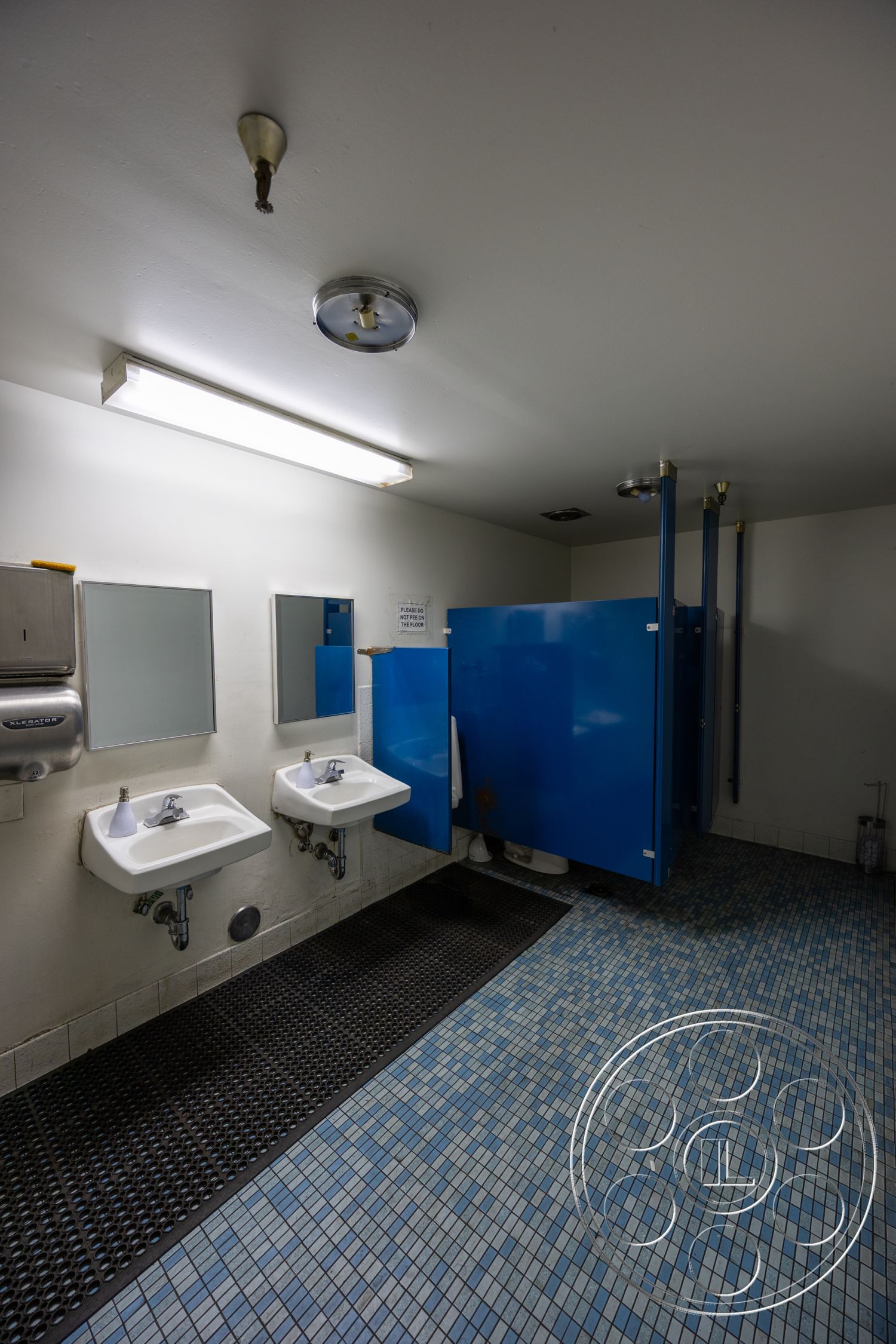 Warehouse 61 - interior bathroom design, high-contrast color scheme, white painted walls, blue partition walls, mosaic tile flooring, sink with chrome faucets, flush ceiling light fixture, wall-mounted hand dryer, vertical restroom mirrors, rubber mat flooring, modern restroom layout