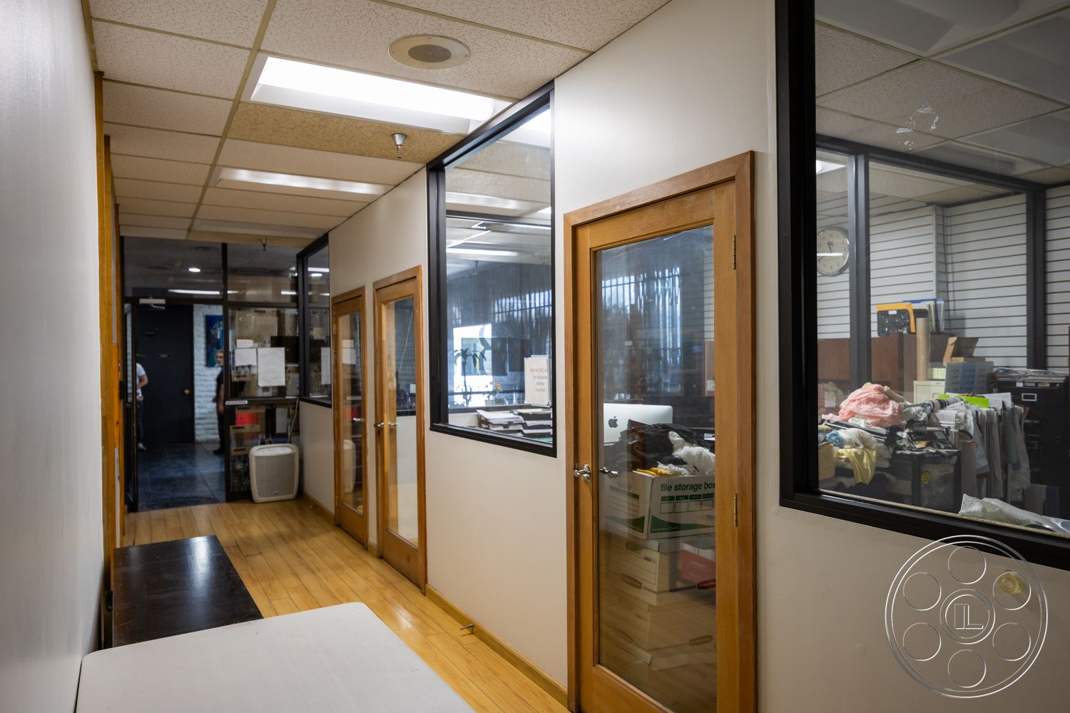 Warehouse 61 - functional workspace, open office layout, spacious corridor, bright fluorescent lighting, glass partition walls, interior hallway, neutral painted walls, modern office design, drop ceiling tiles, wooden door frames, vinyl tile flooring, black wall paneling, administrative office space, windows with black aluminum frames, cluttered office environment