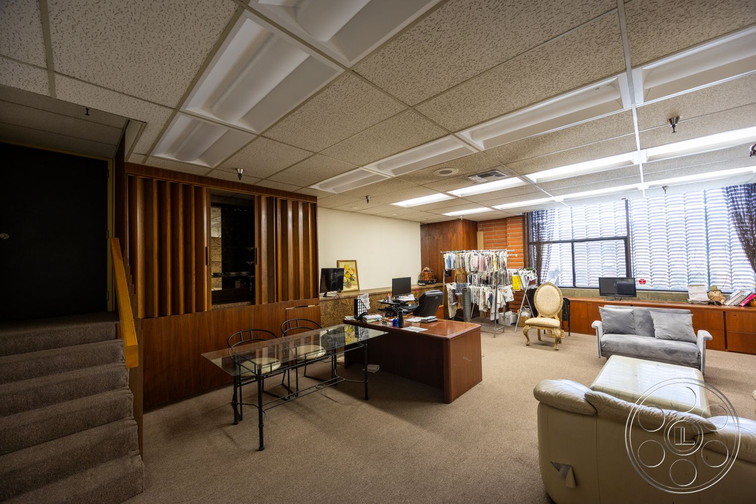Warehouse 61 - functional workspace, carpet flooring, natural light from large windows, textured wall treatment, upholstered armchair, open layout design, interior office space, fiberboard ceiling tiles, exposed wood paneling, glass-top desk, wooden office cabinetry, computer workstation area, window treatment with vertical blinds, curved modern sofa, staircase with carpeted steps, multifunctional room, adaptable office setting, work and leisure area, home office environment