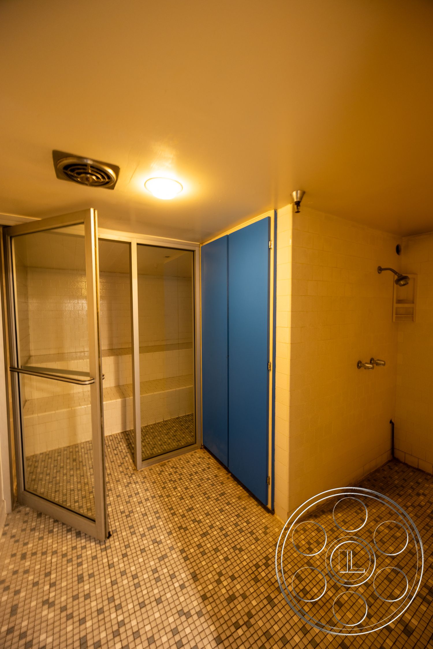 Warehouse 61 - white tiled walls, glass shower doors, ambient ceiling lighting, mosaic tile flooring, interior shower room, blue privacy panels, stainless steel shower fixtures, exposed ceiling ventilation