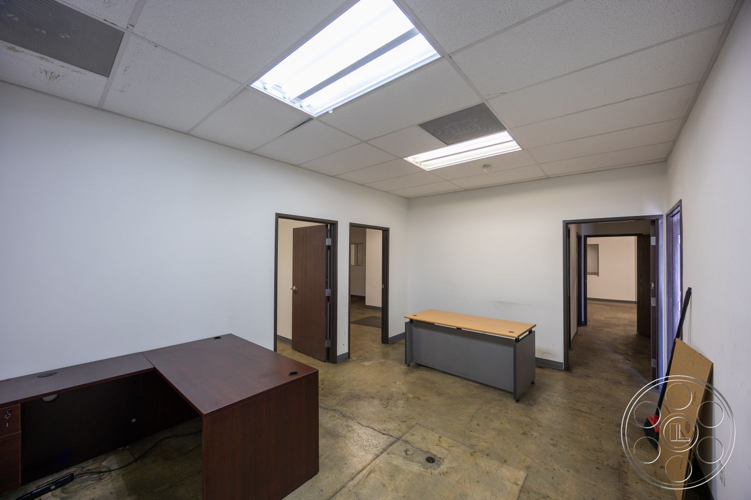 Warehouse 61 - neutral color palette, functional workspace, commercial space, exposed concrete floor, minimalist design details, white painted walls, interior office environment, drop ceiling with fluorescent lighting, office space layout, dark wood paneling on door frames, storage room access, square room shape, basic office furnishings, multiple door entries