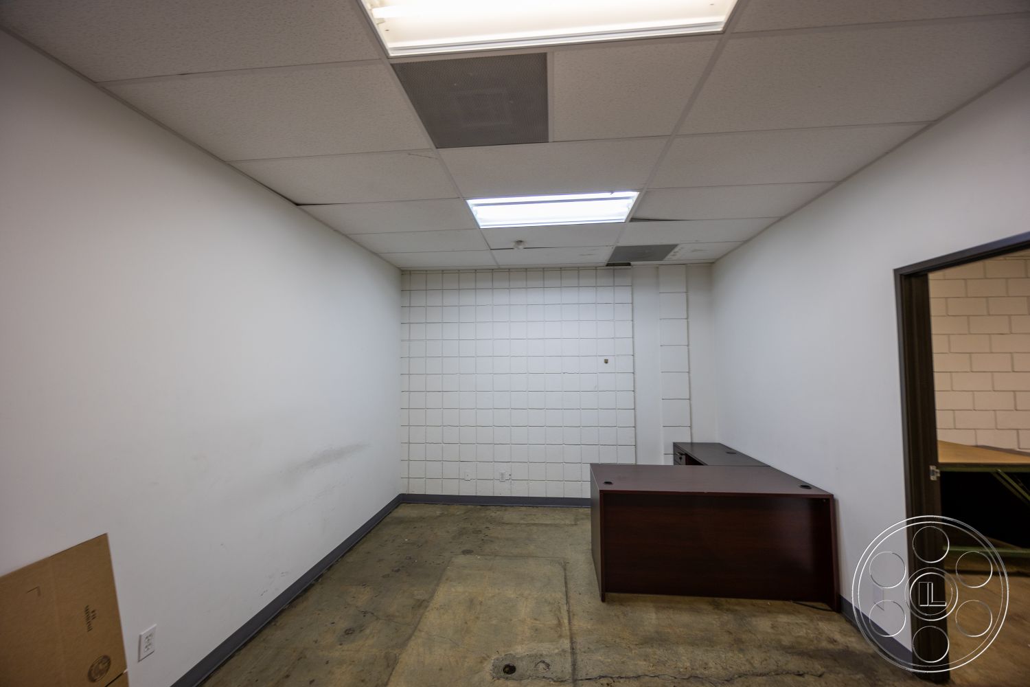 Warehouse 61 - neutral color palette, minimalist design elements, functional workspace, exposed concrete floor, white painted walls, interior office space, drop ceiling tiles, suspension lighting fixtures, dark wood office desk, paneling finish on one wall