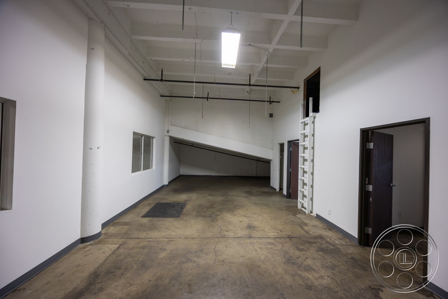 Warehouse 61 - metal lighting fixtures, functional workspace, large industrial windows, concrete columns, commercial interior, open floor plan layout, white painted walls, exposed concrete flooring, high ceilings with exposed beams, interior space with minimalist design, sloped floor transition, dark wood door frames, rectangular floor space, modern industrial aesthetic