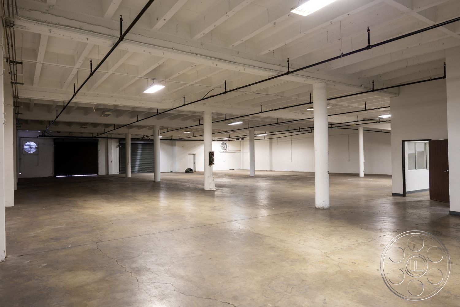 Warehouse 61 - floor-to-ceiling windows, ventilation ducts, exposed concrete floor, bright fluorescent lighting, open layout design, steel support columns, urban industrial setting, interior warehouse space, white painted concrete walls, industrial ceiling with exposed beams, large rolling garage door, minimalist interior space, rough texture surfaces, flexible multipurpose area, sprinkler system infrastructure, concrete block partition wall