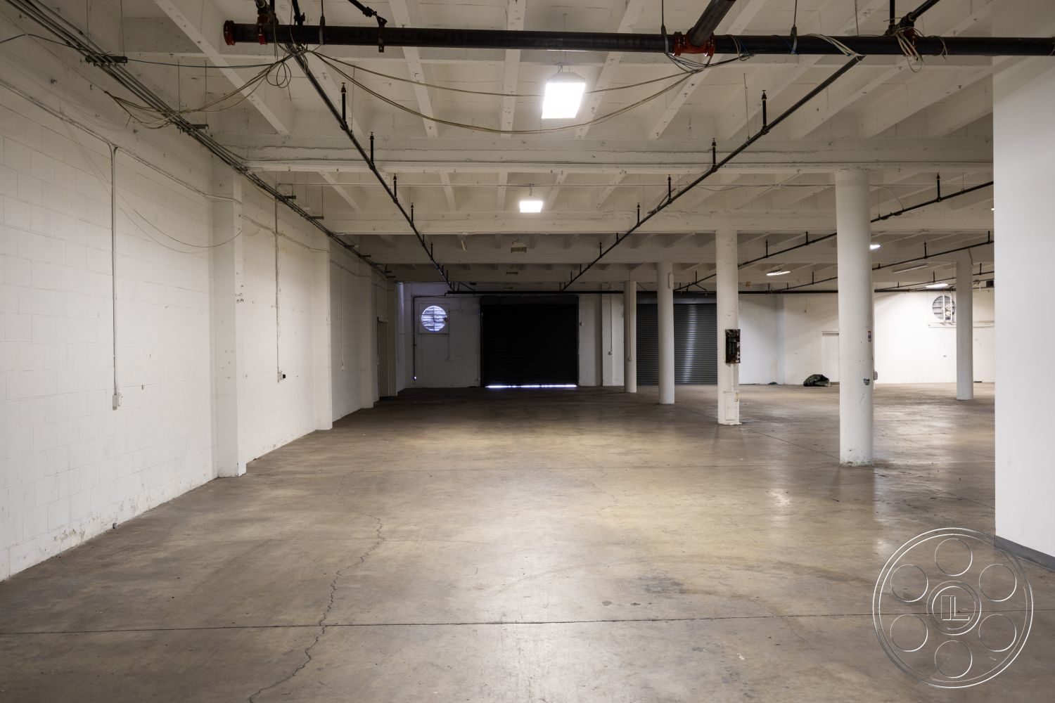 Warehouse 61 - neutral color palette, minimalist design, open floor plan, floor-to-ceiling windows, large roll-up door, metal support columns, exposed wooden ceiling beams, exposed concrete flooring, white painted concrete walls, industrial ceiling lights, urban industrial space, interior warehouse setting, high ceiling architecture