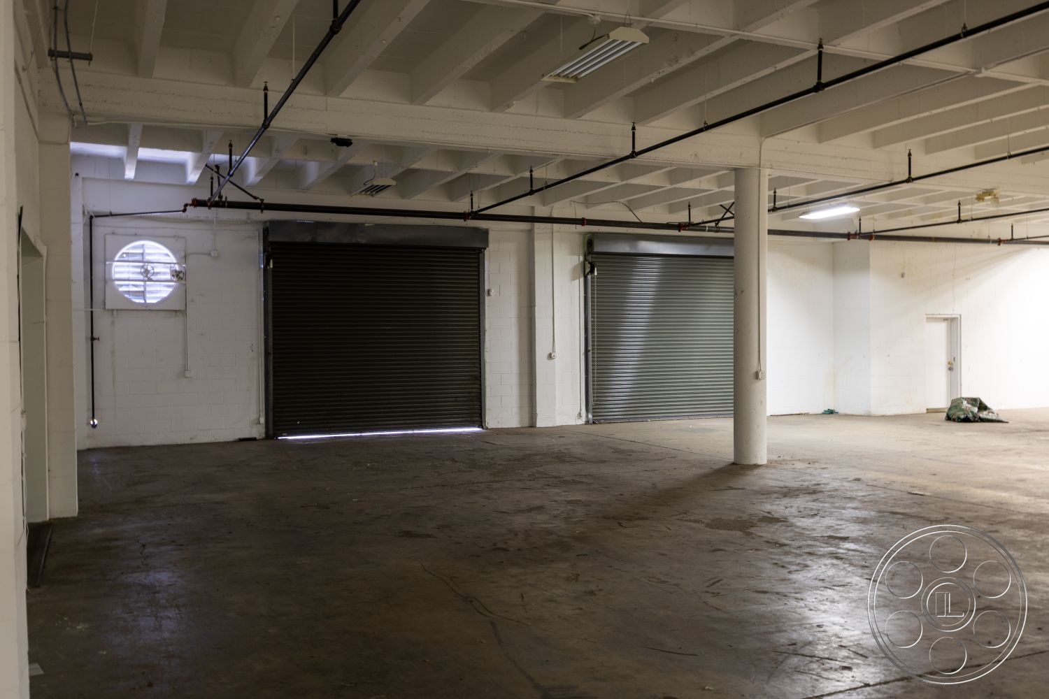 Warehouse 61 - high ceilings, concrete flooring, exposed concrete walls, urban setting, white painted walls, open floor plan interior, metal roll-up doors, industrial ceiling structure, square window openings, exposed piped ceiling, minimalist industrial design, raw space for customization, flexible workspace design