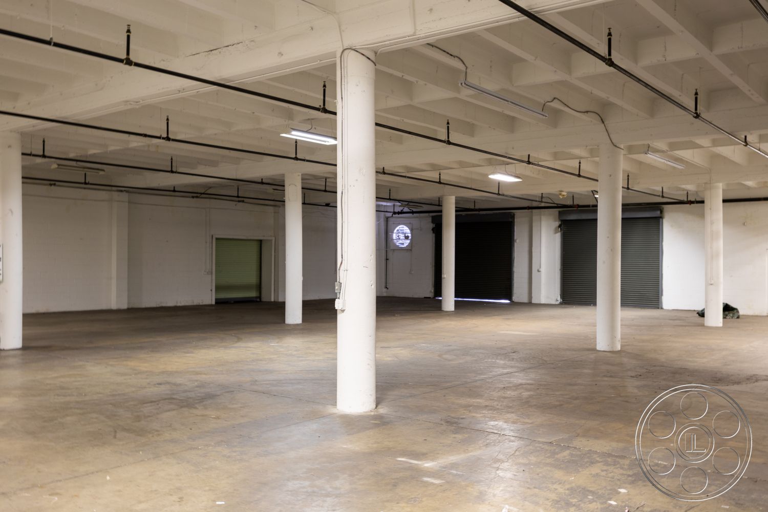 Warehouse 61 - neutral color palette, open floor plan, concrete block walls, industrial lighting fixtures, commercial space, natural light from windows, white painted walls, steel support columns, flexible workspace layout, high ceilings with exposed beams, exposed concrete floors, large roll-up garage doors, warehouse space interior, minimalistic industrial style, urban loft aesthetic