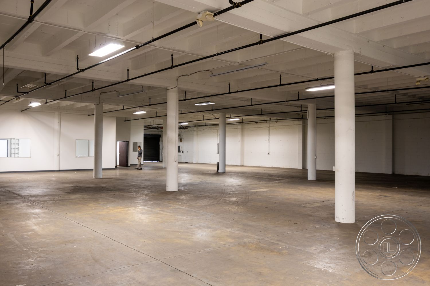 Warehouse 61 - minimalist design, functional workspace, exposed concrete ceiling, large warehouse space, white painted walls, open floor plan interior, fluorescent lighting fixtures, commercial building setting, unpolished concrete floor, industrial-style columns, urban industrial interior, unfinished space for renovation, versatile layout for multiple uses